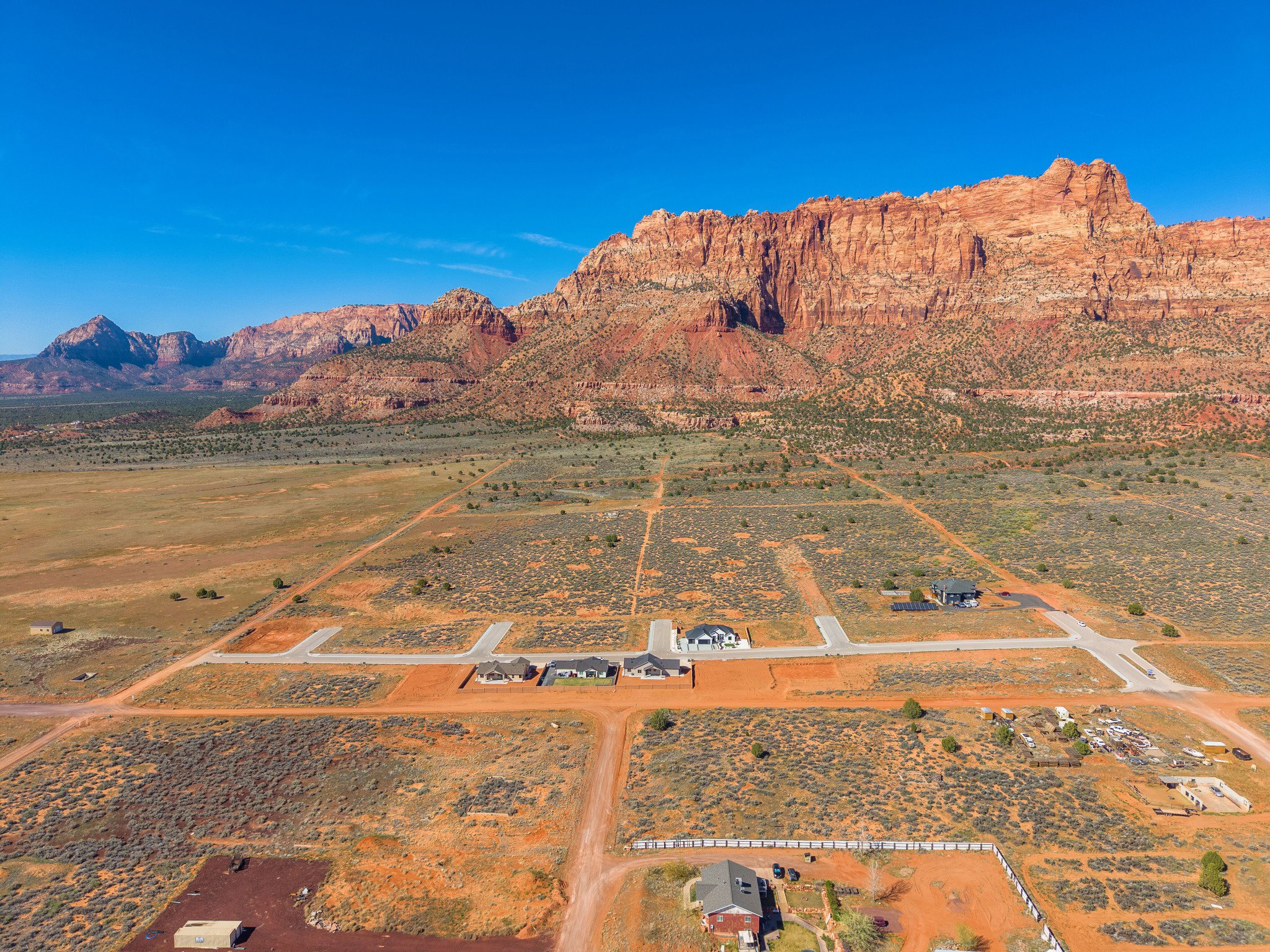 Expansive desert landscape featuring red rock mountain formations and a developing residential area with paved roads
