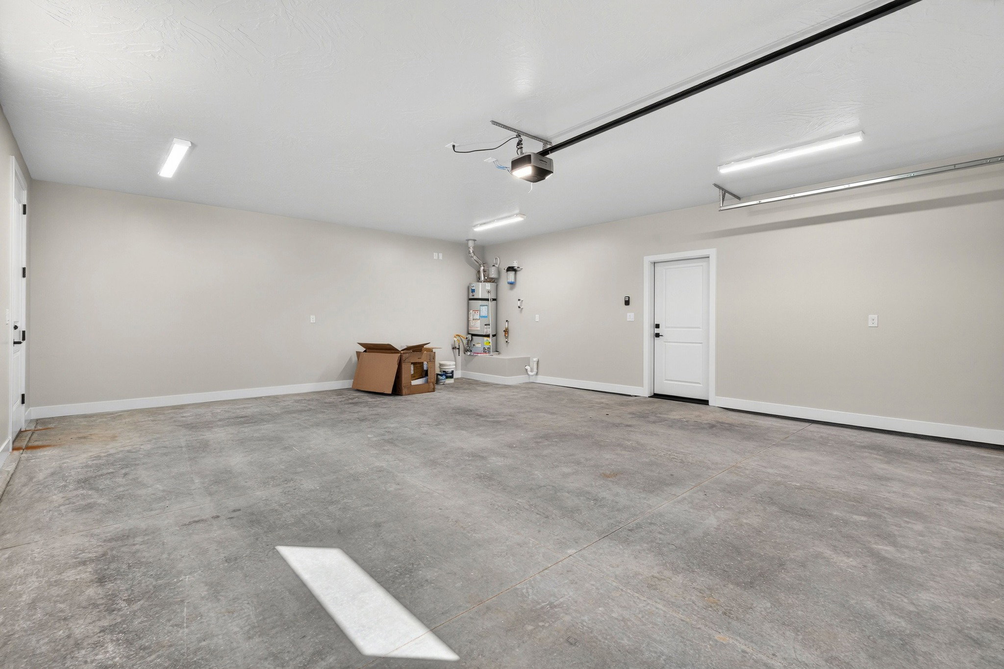 Spacious garage featuring a concrete floor, two white entry doors, and overhead linear lighting fixtures