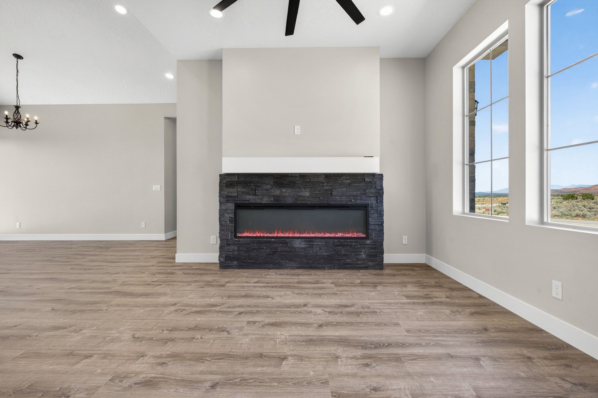 Spacious interior featuring a stacked stone fireplace with an electric insert, wood-finish flooring, recessed lighting, and large windows