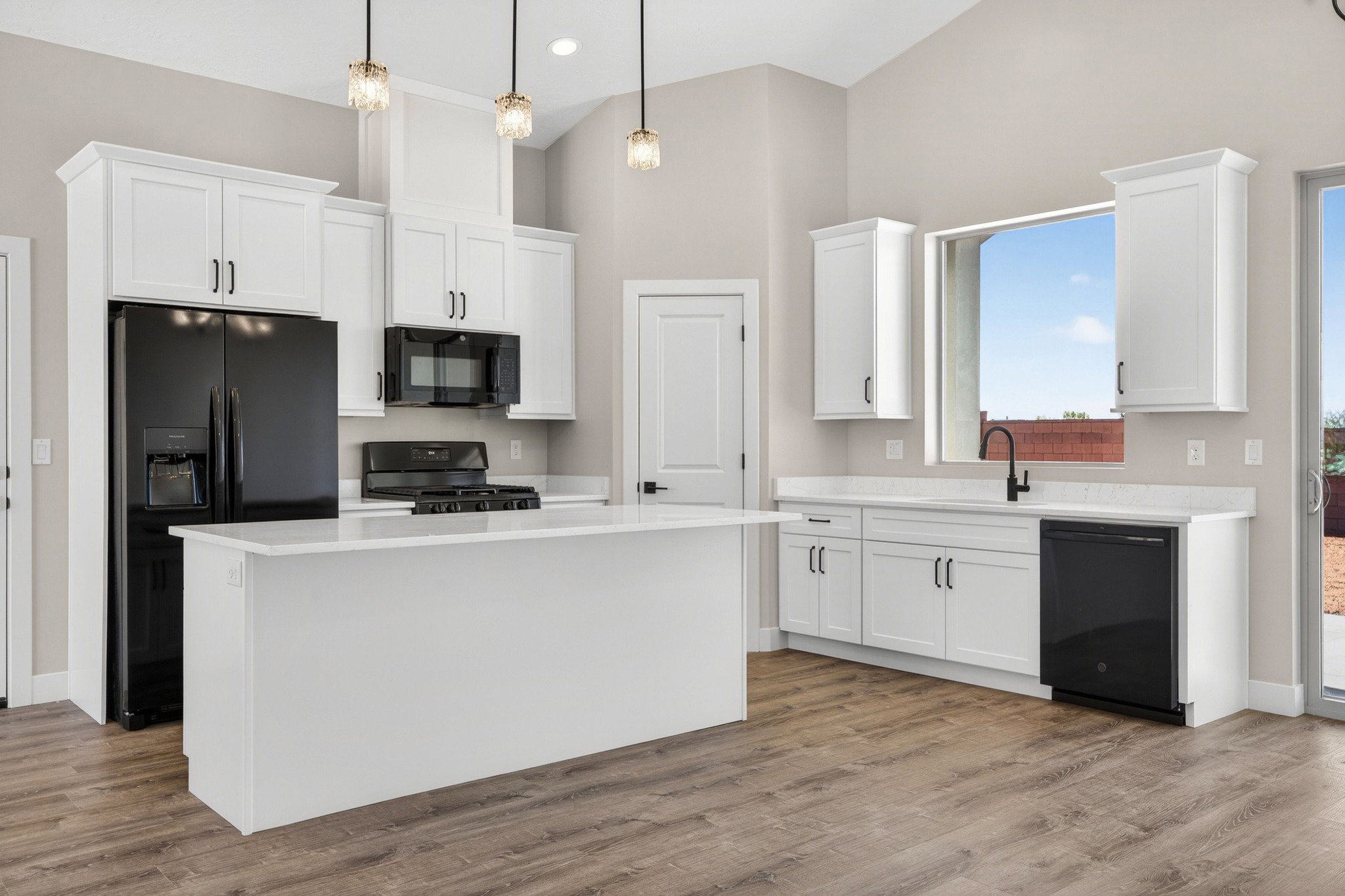 Open-concept kitchen featuring an island, white cabinetry, black appliances, wood-finish flooring, and vaulted ceilings with pendant lighting