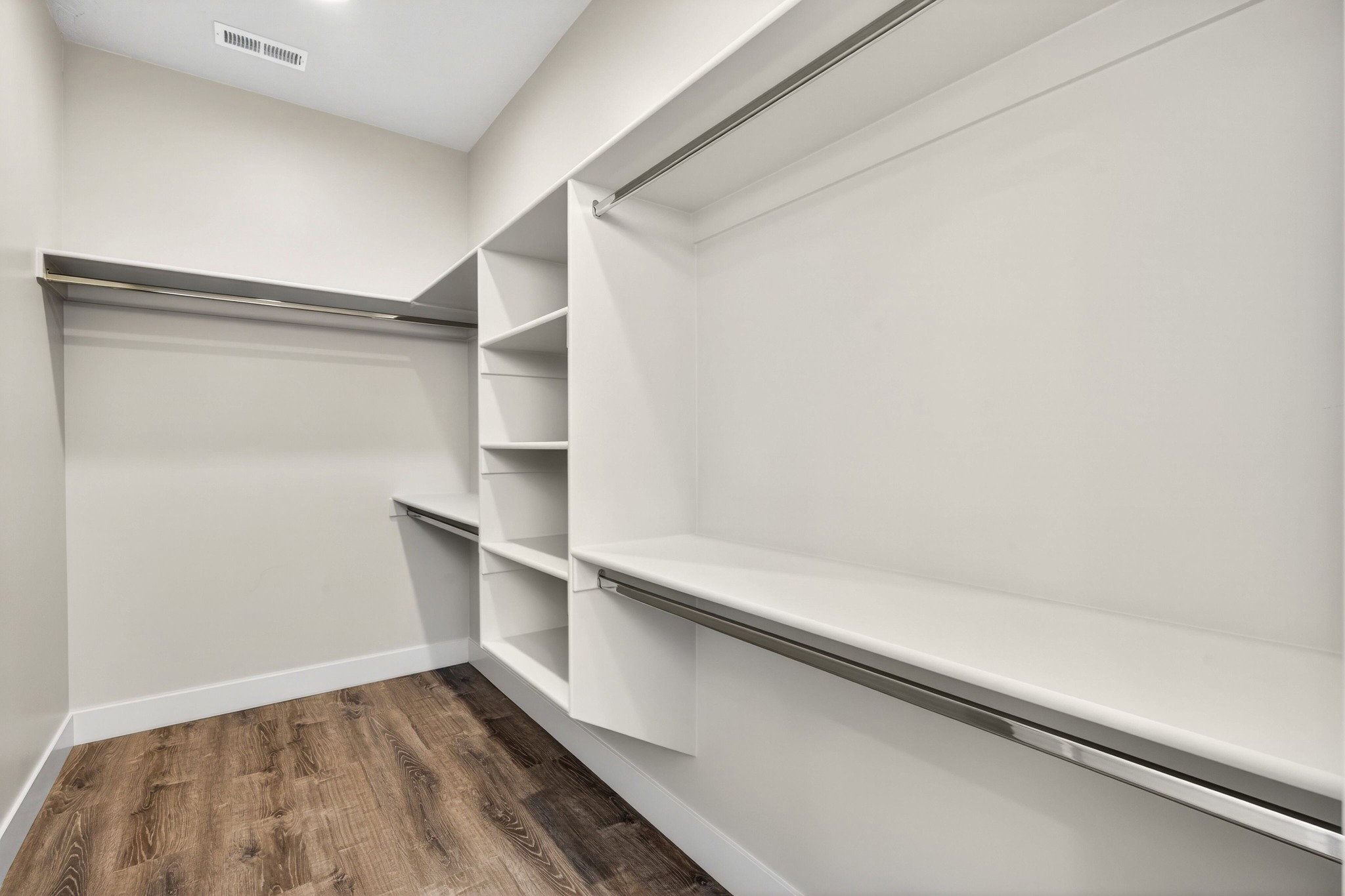 Walk-in closet featuring wood-finish flooring, built-in shelving, and multiple clothing rods