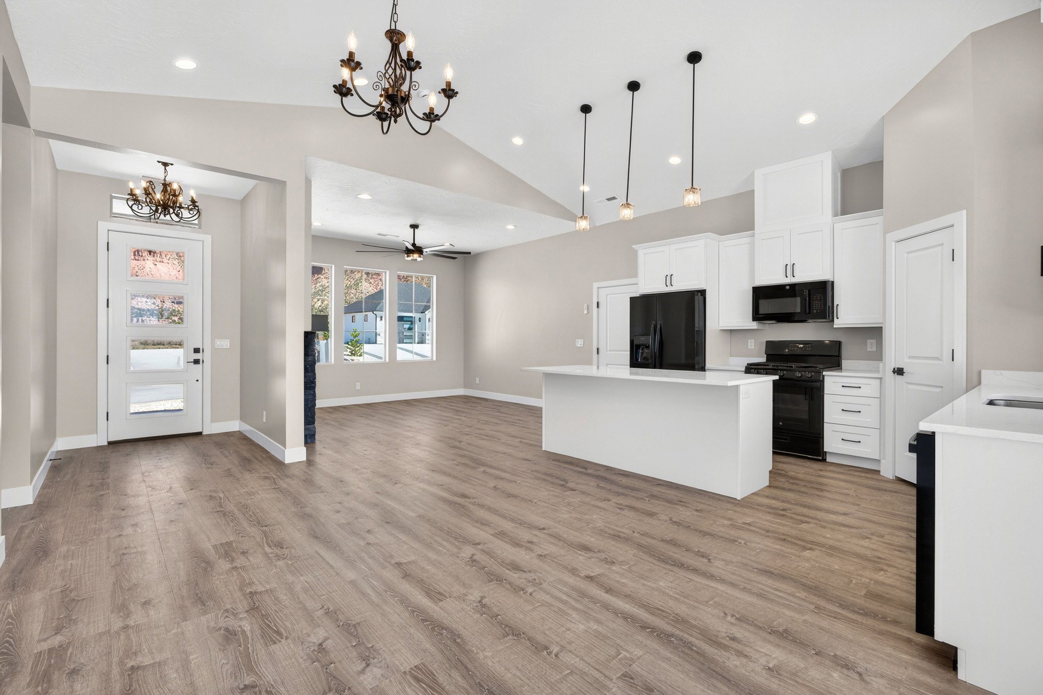 Open-concept living space featuring vaulted ceilings, wood-finish flooring, a kitchen island with pendant lighting, white cabinetry, and black appliances