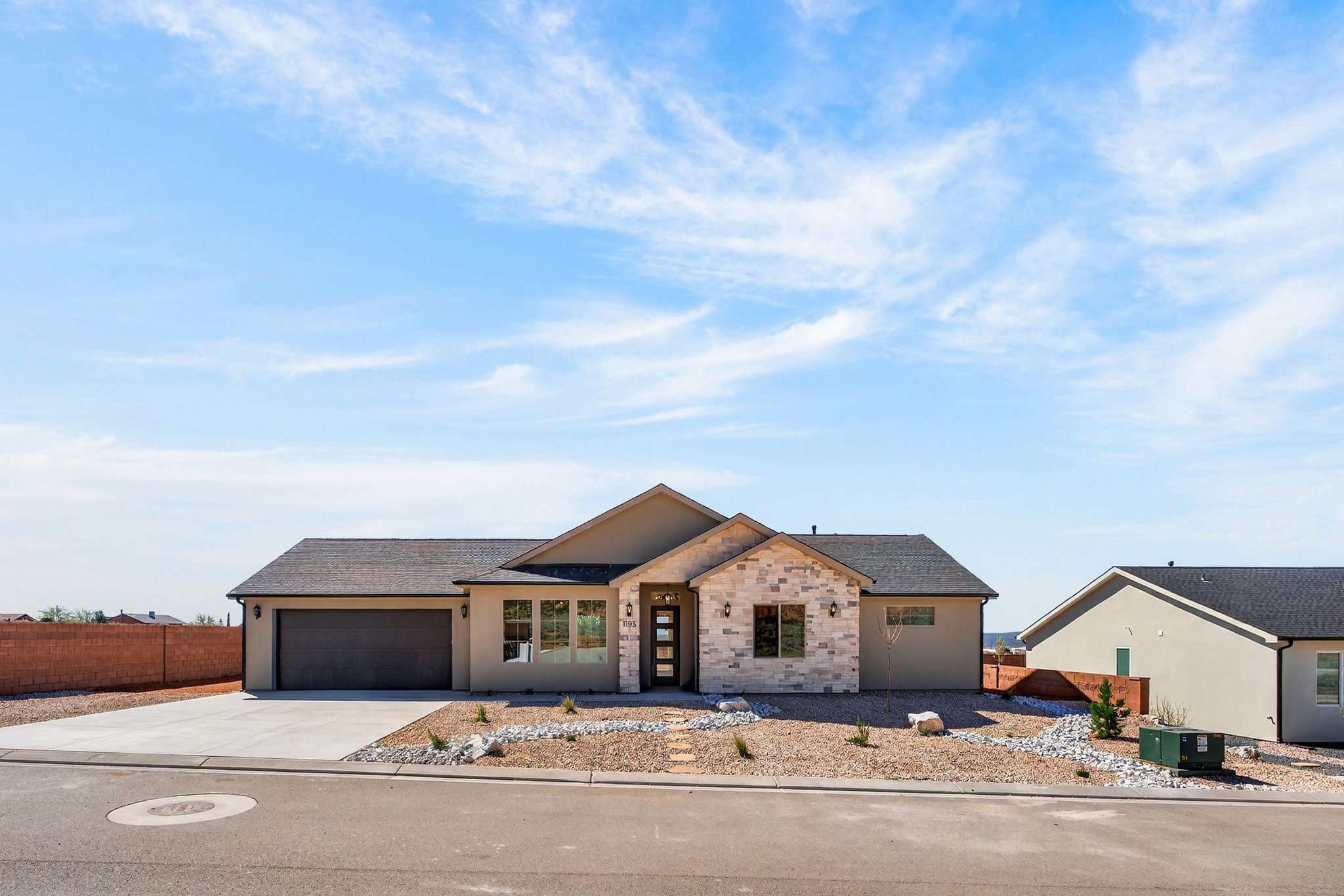 Contemporary stucco exterior with stone accents, dark asphalt shingle roof, integrated two-car garage, and desert-adapted landscaping