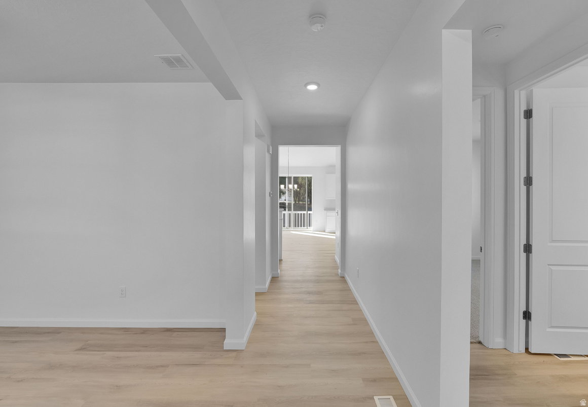 Light wood-finish flooring extending through an open hallway with bright white walls