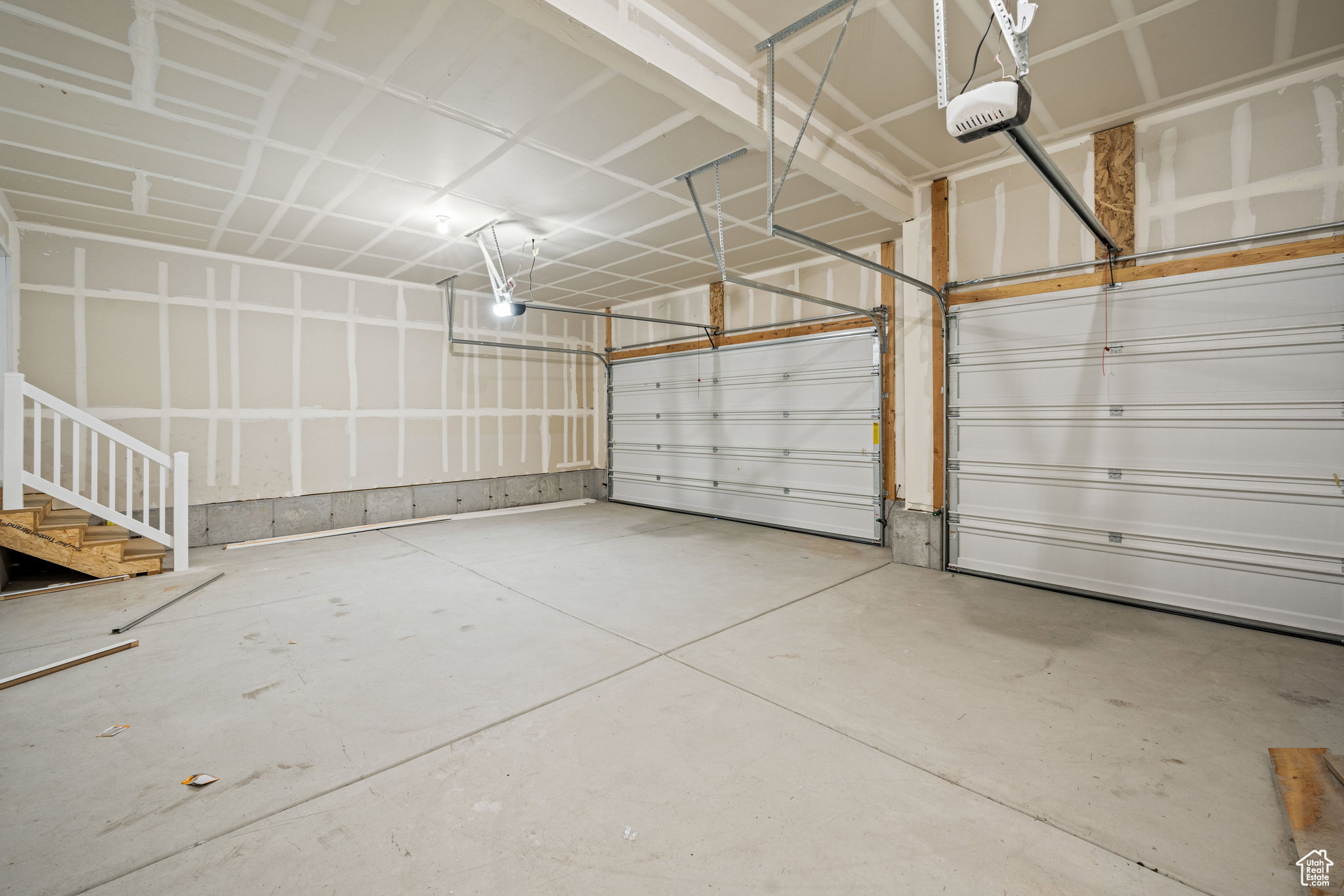 Two-car garage featuring a concrete floor, two white garage doors, and unfinished drywall walls