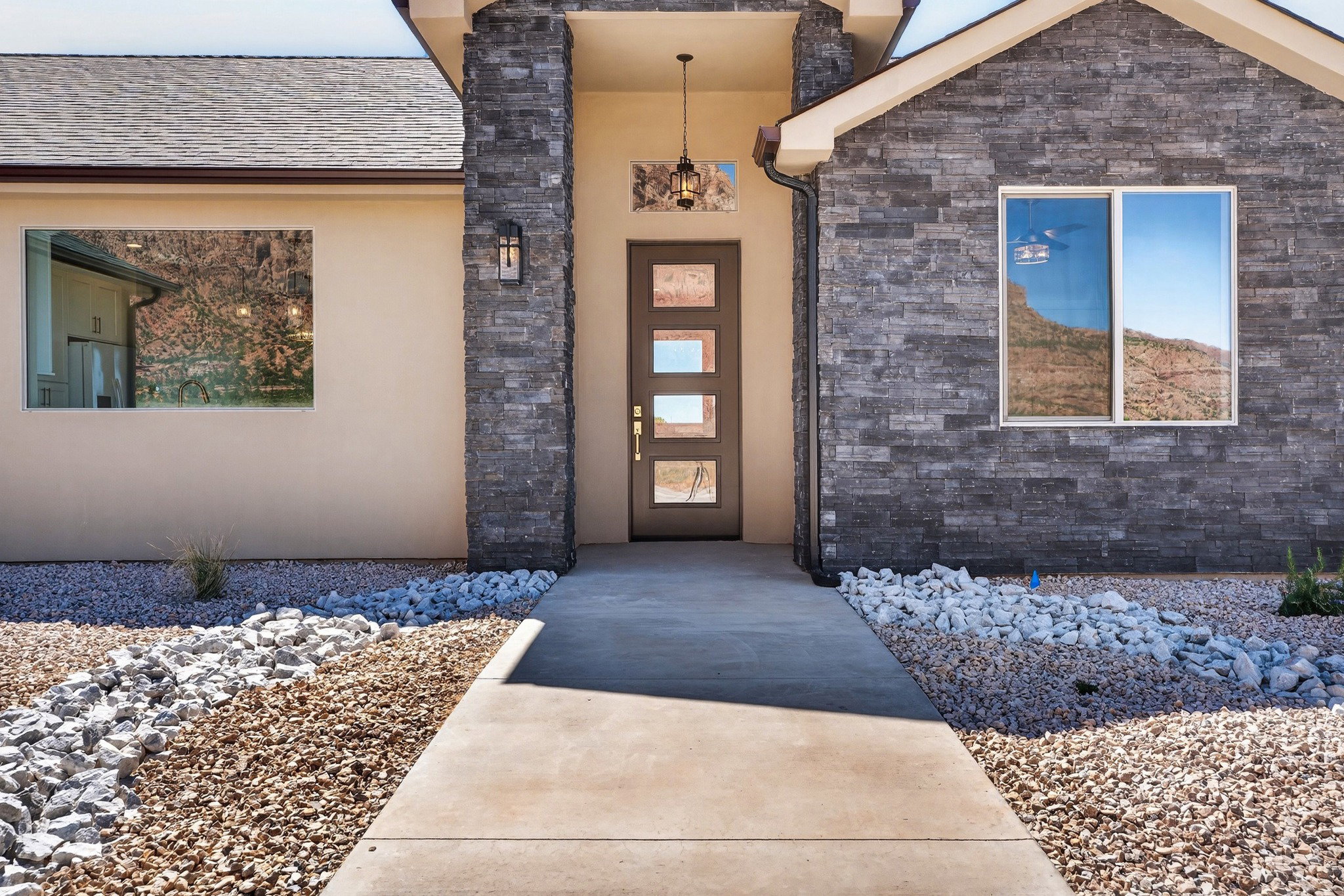 Entryway featuring a modern door with multiple glass panes, stucco and stone veneer exterior finishes, an outdoor wall sconce, and a concrete walkway