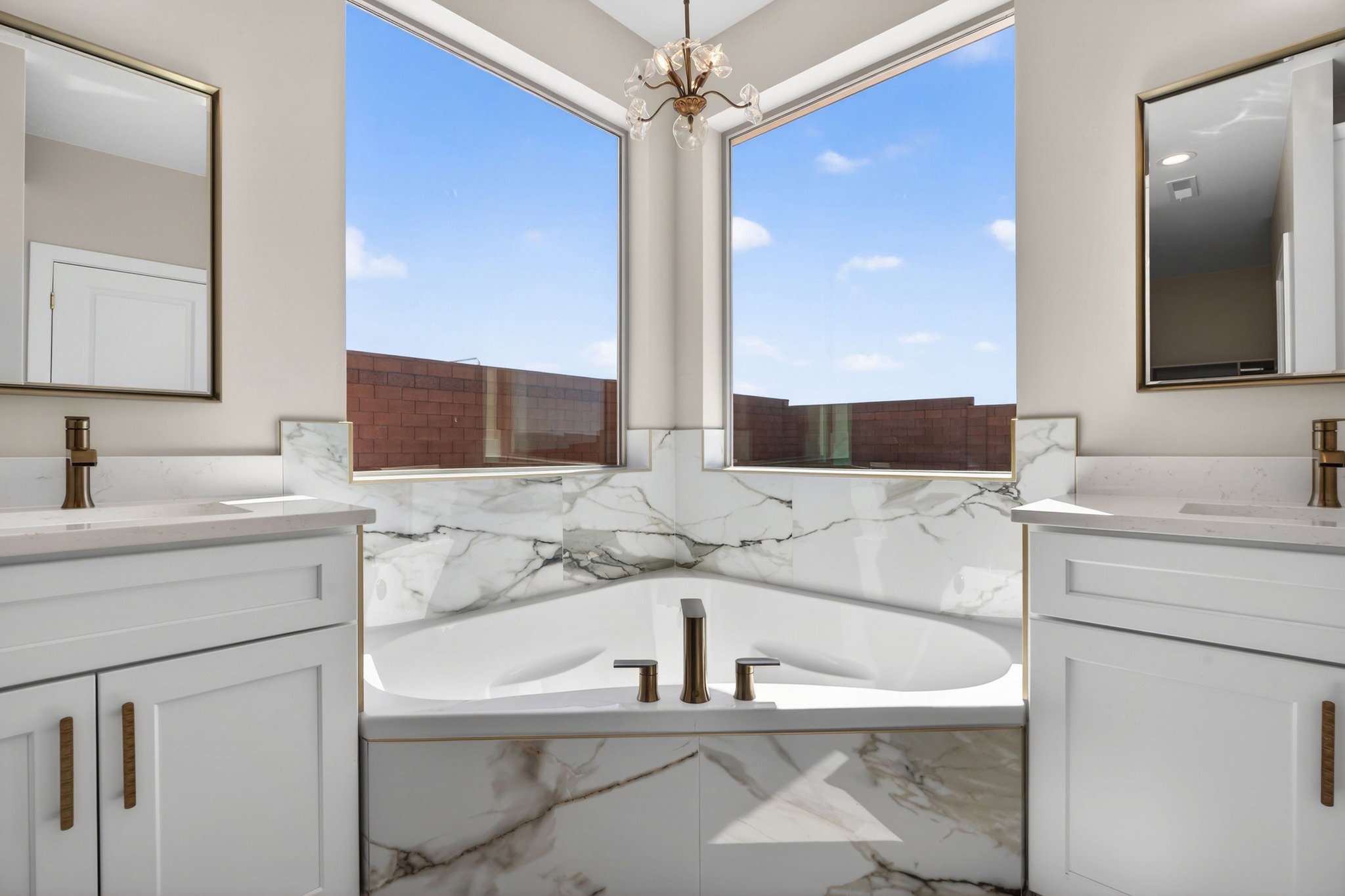 Freestanding soaking tub with a surrounding marble-finish enclosure, dual rectangular windows, and a brass-tone chandelier