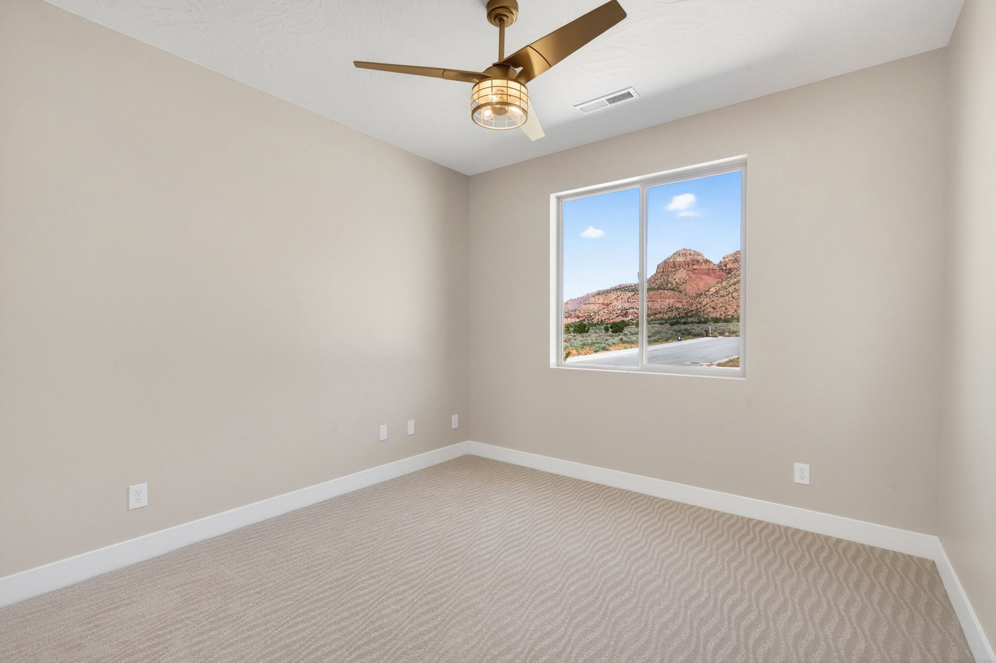 Spacious room featuring neutral-toned walls, patterned carpet flooring, a contemporary ceiling fan with integrated lighting, and a large window offering mountain scenery