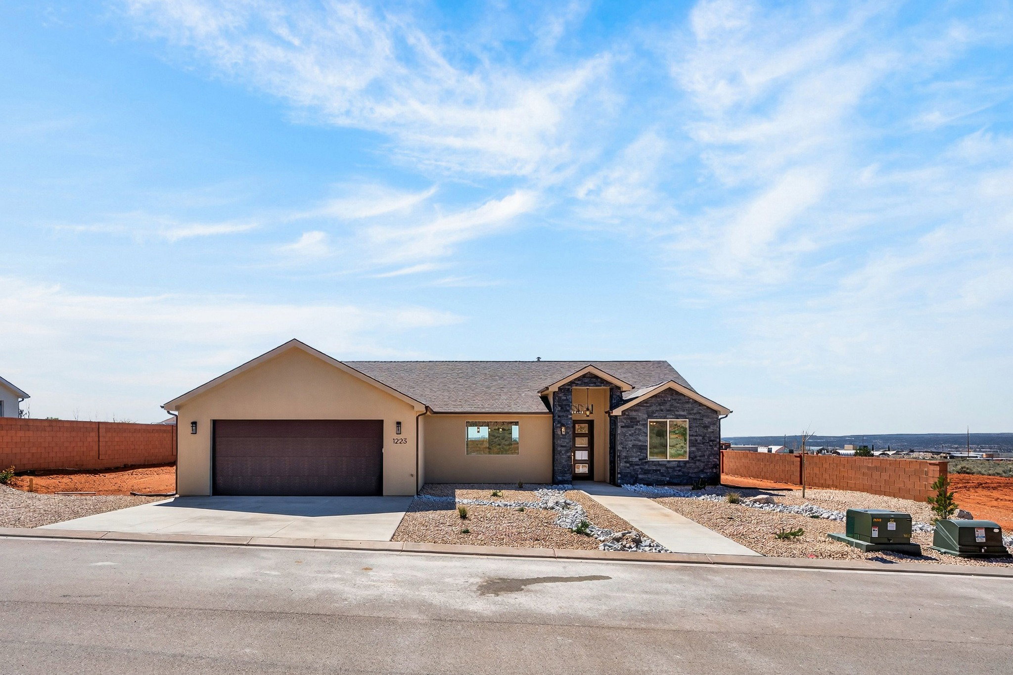 Modern stucco and stone exterior featuring a two-car garage, a contemporary front door with vertical window panels, and a stone facade accent