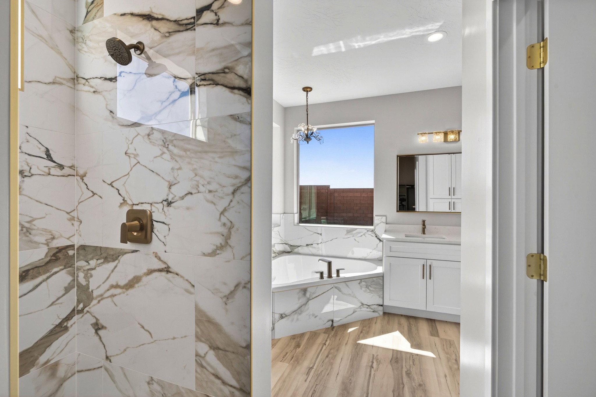 Spacious bathroom featuring a glass-enclosed shower with large format marble-look tile, a separate built-in soaking tub, wood-finish flooring, a white vanity with a rectangular sink, and a built-in medicine cabinet