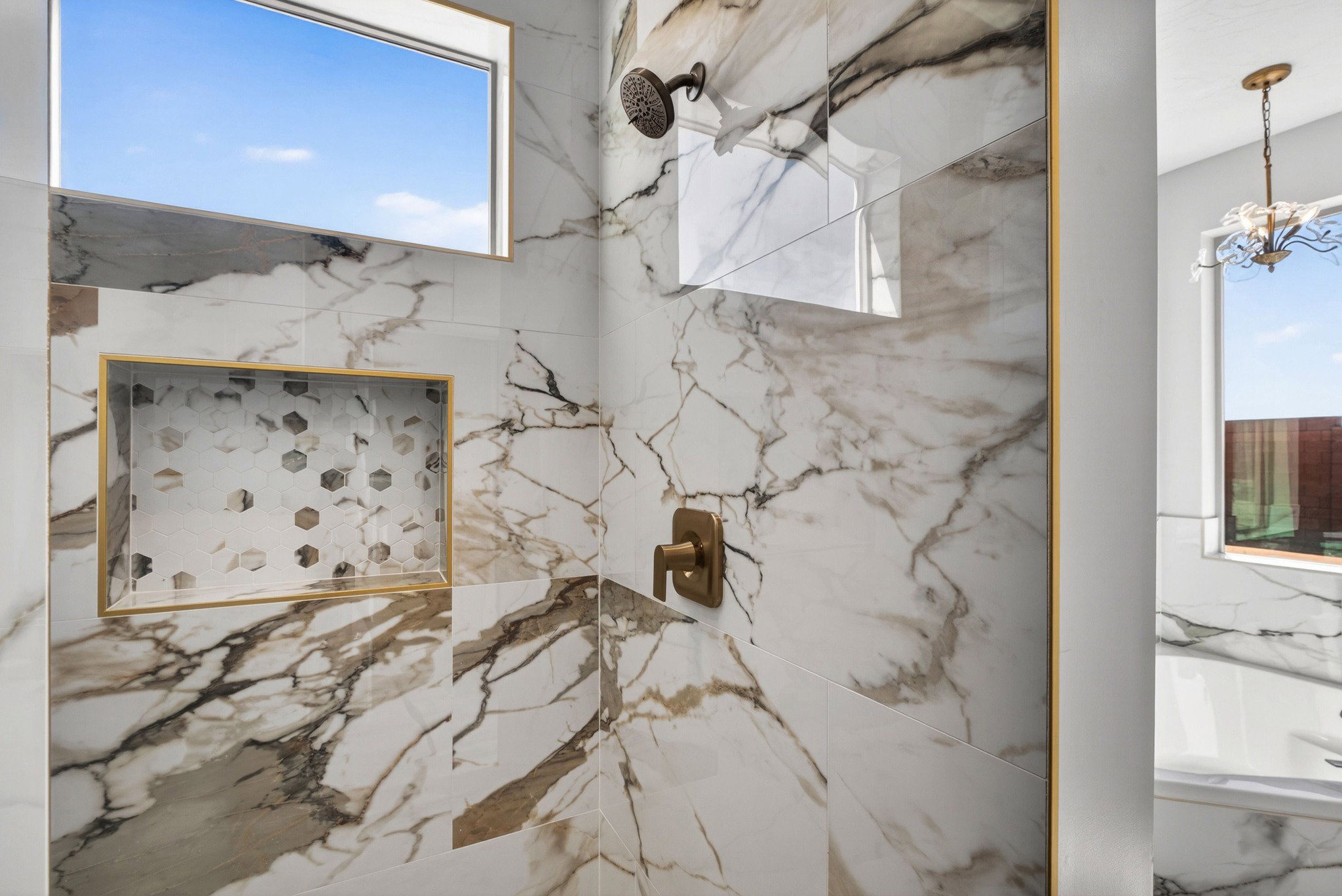 Shower featuring large-format marbled tile, a built-in shower niche with mosaic tile inlay and gold-tone trim, a bronze-finish showerhead, and a bronze-finish control lever