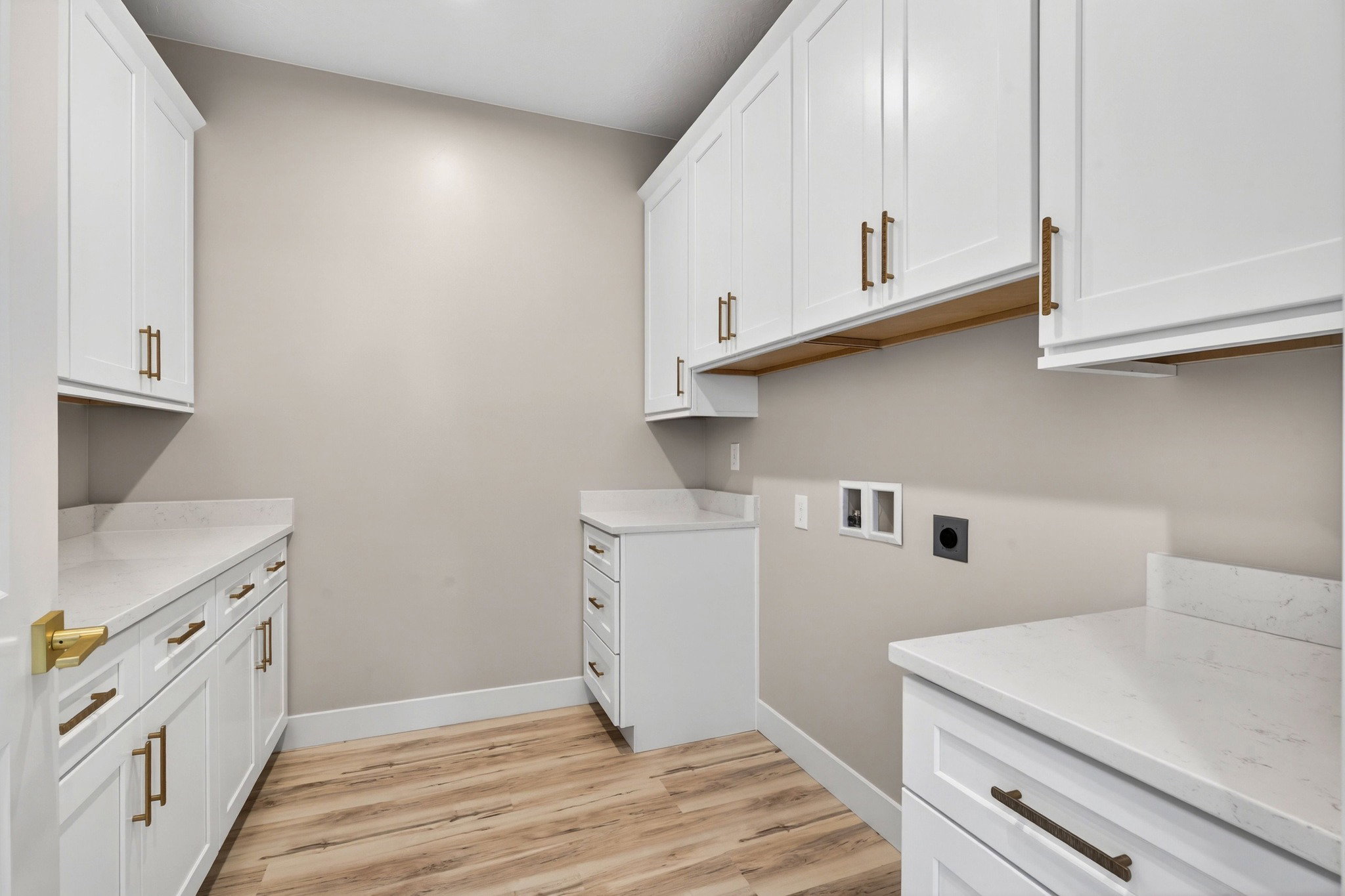 Dedicated utility room featuring extensive white cabinetry, light-toned countertops, wood-finish flooring, and a laundry hookup