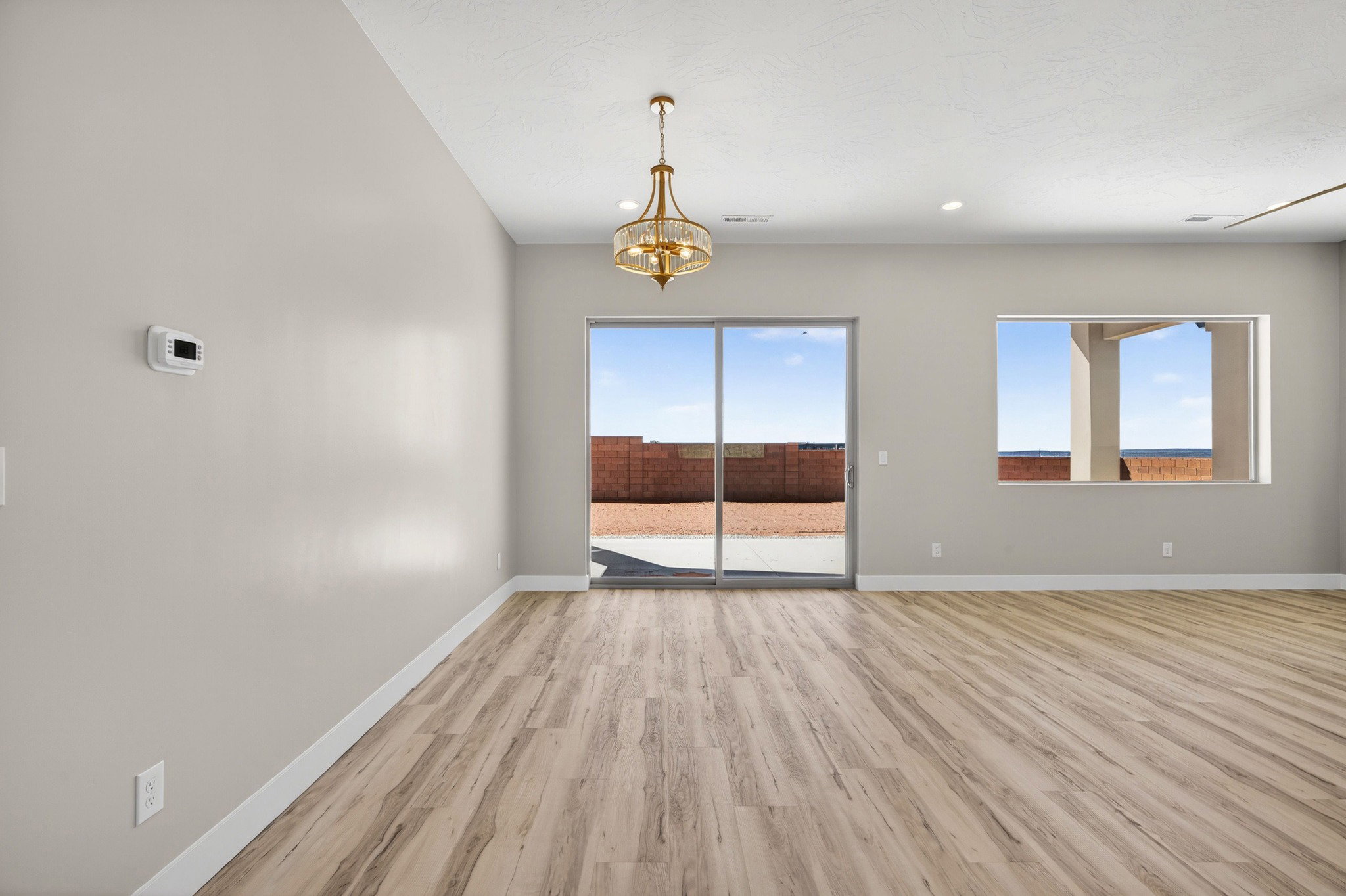Spacious interior room featuring wood-finish flooring, light-toned walls, and a contemporary chandelier