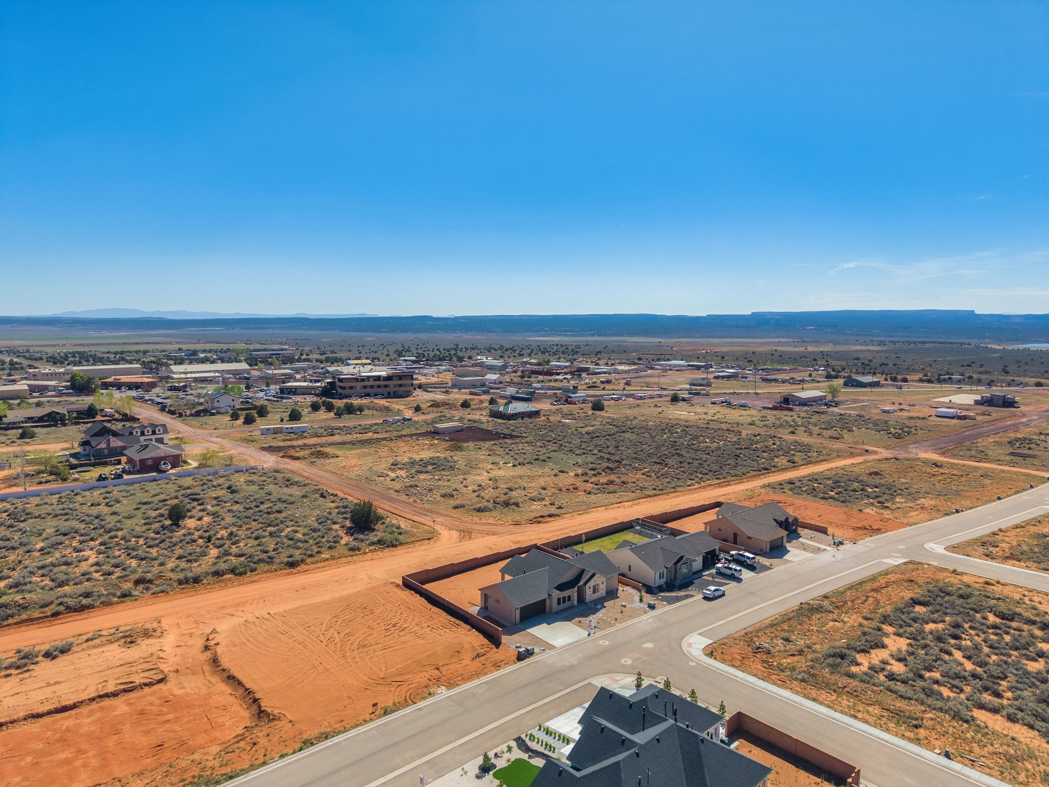 New construction residences featuring light-colored stucco exteriors and dark roofing, situated on spacious red earth lots