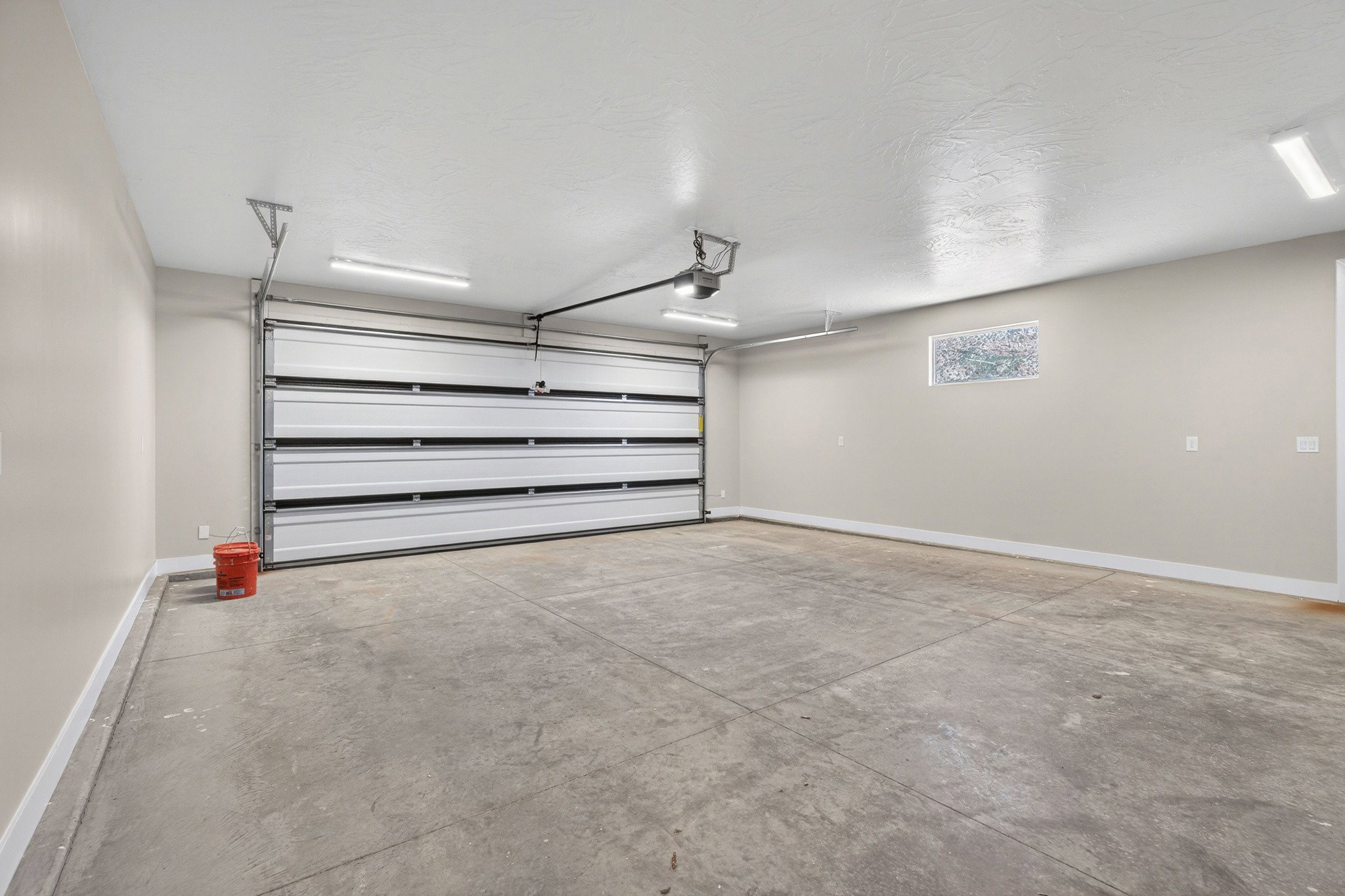 Spacious garage featuring a sectional overhead door, concrete flooring, ample overhead lighting, and a frosted transom window