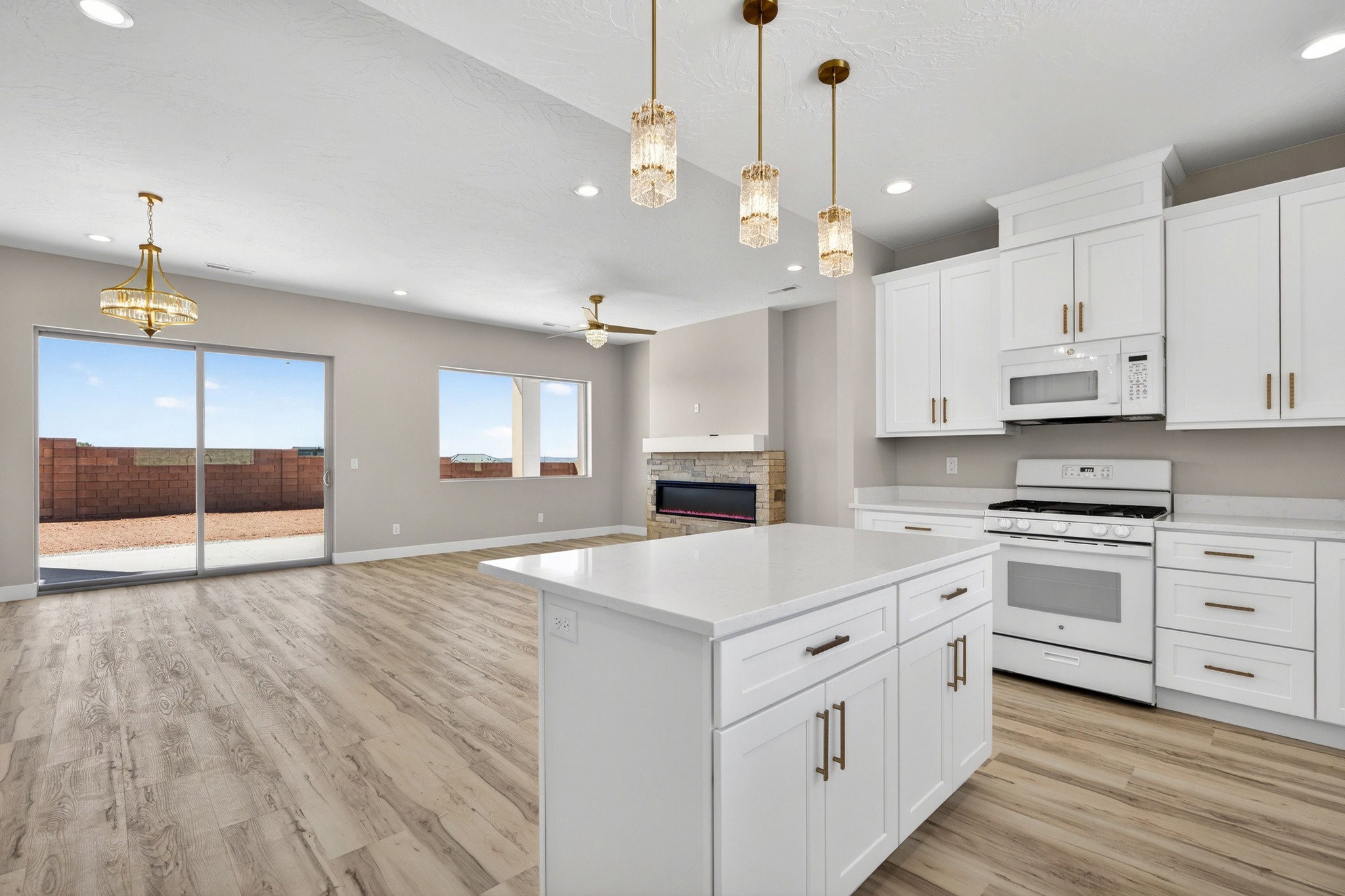 Spacious kitchen featuring an expansive island with a pristine countertop, white cabinetry with brushed bronze hardware, and pendant lighting