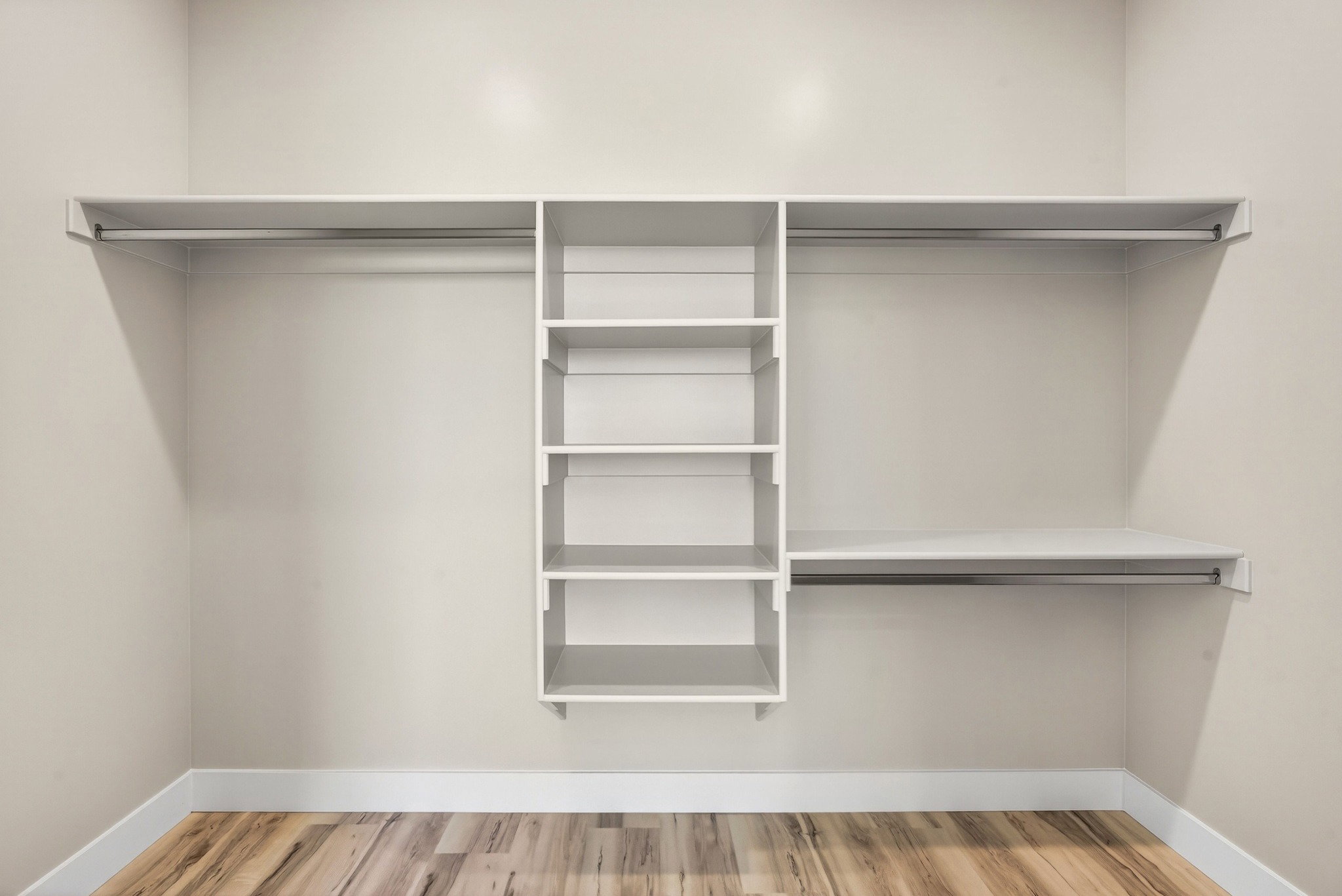 Custom closet system featuring multiple hanging rods, integrated shelving units, and wood-finish flooring
