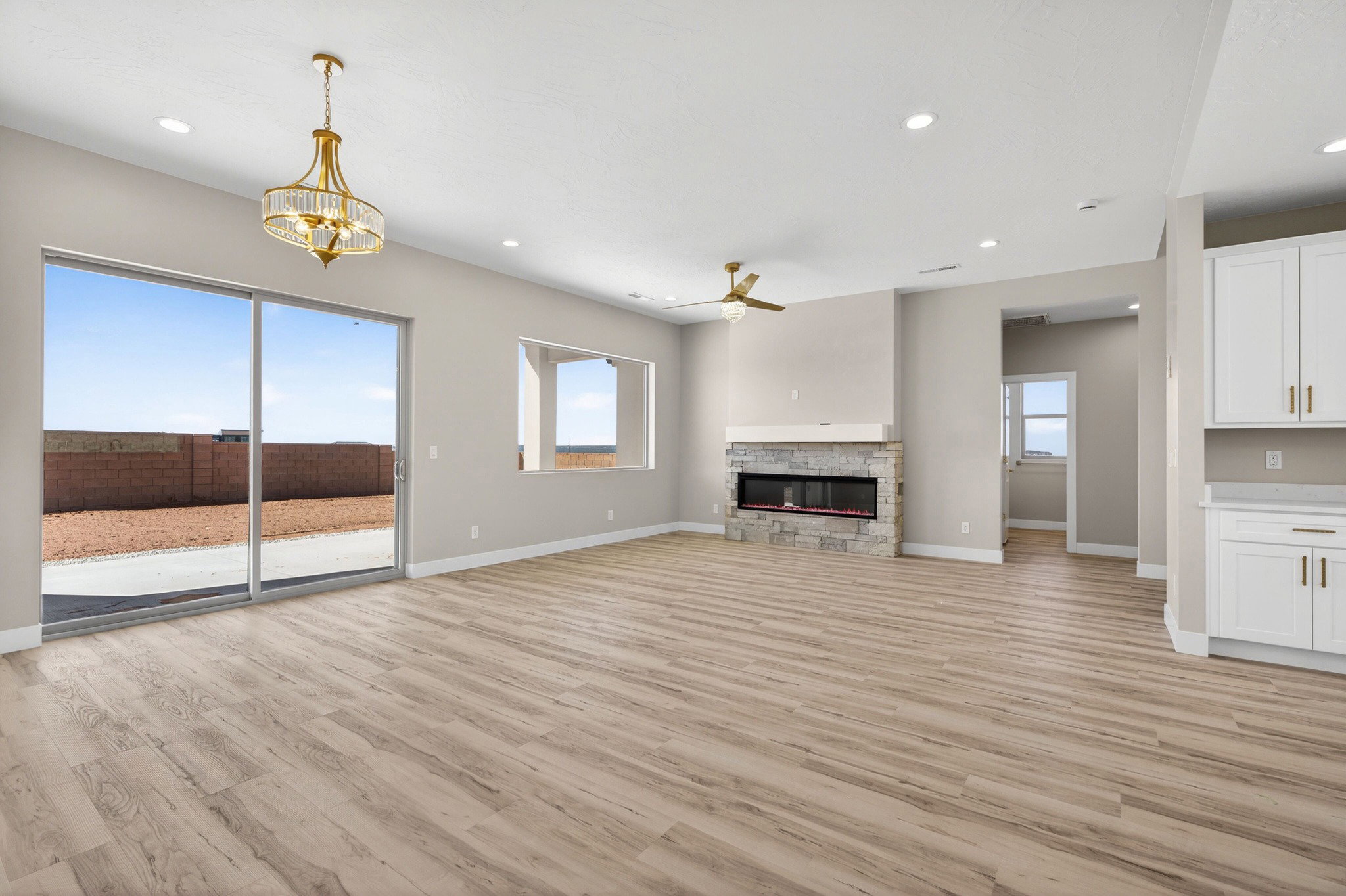 Spacious living area featuring wood-finish flooring, a stone-clad fireplace with a mantel, and a ceiling fan
