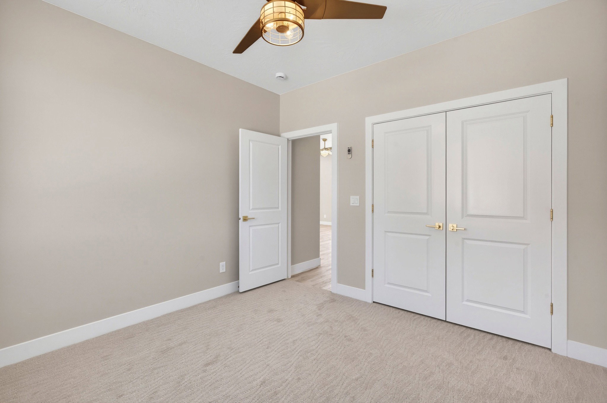 Carpeted room featuring a ceiling fan with integrated lighting, a single paneled door, and double paneled doors with brass hardware