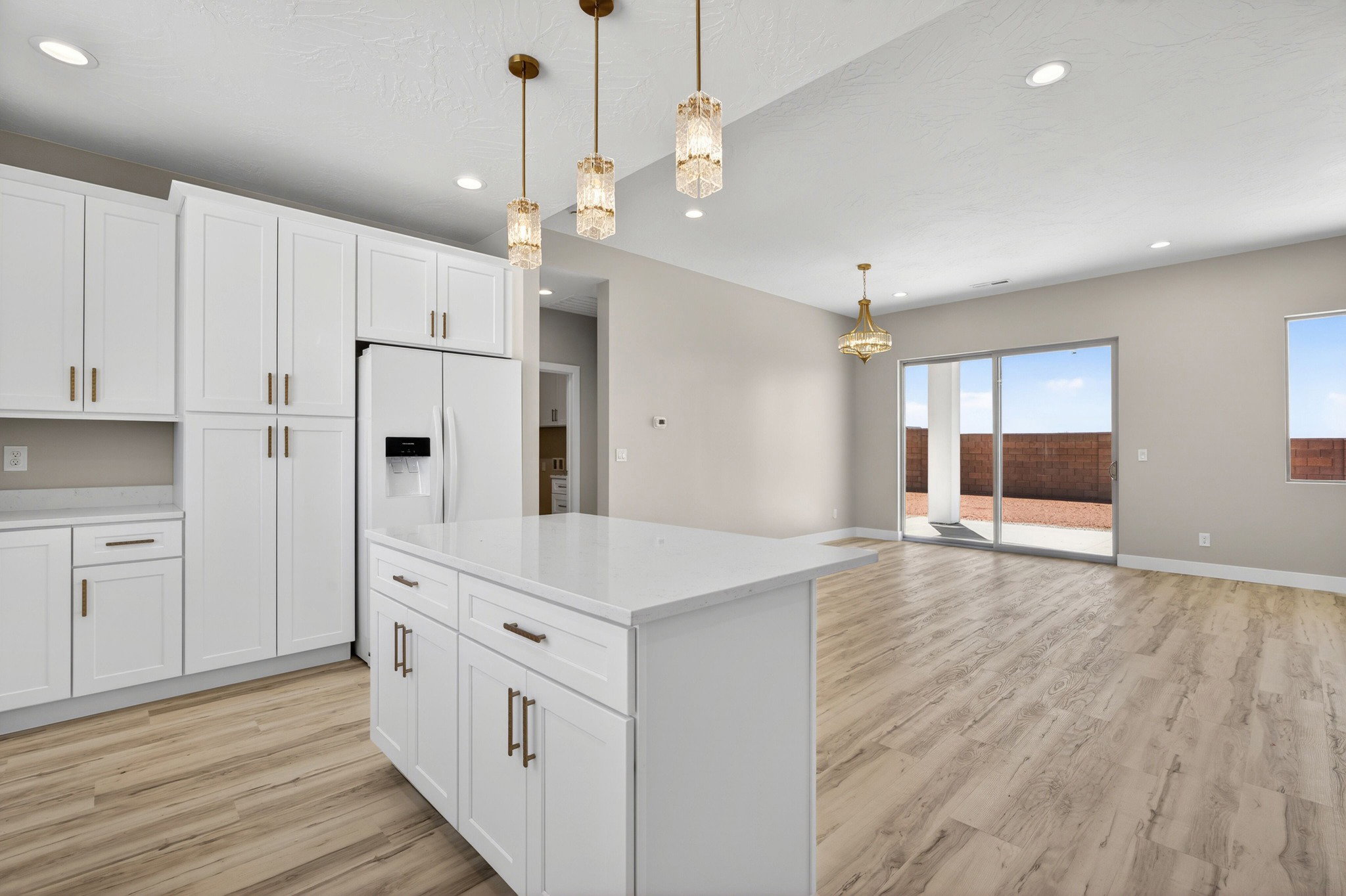 Open-concept kitchen and living area featuring white shaker cabinetry, an island with a light-toned countertop, and wood-finish flooring