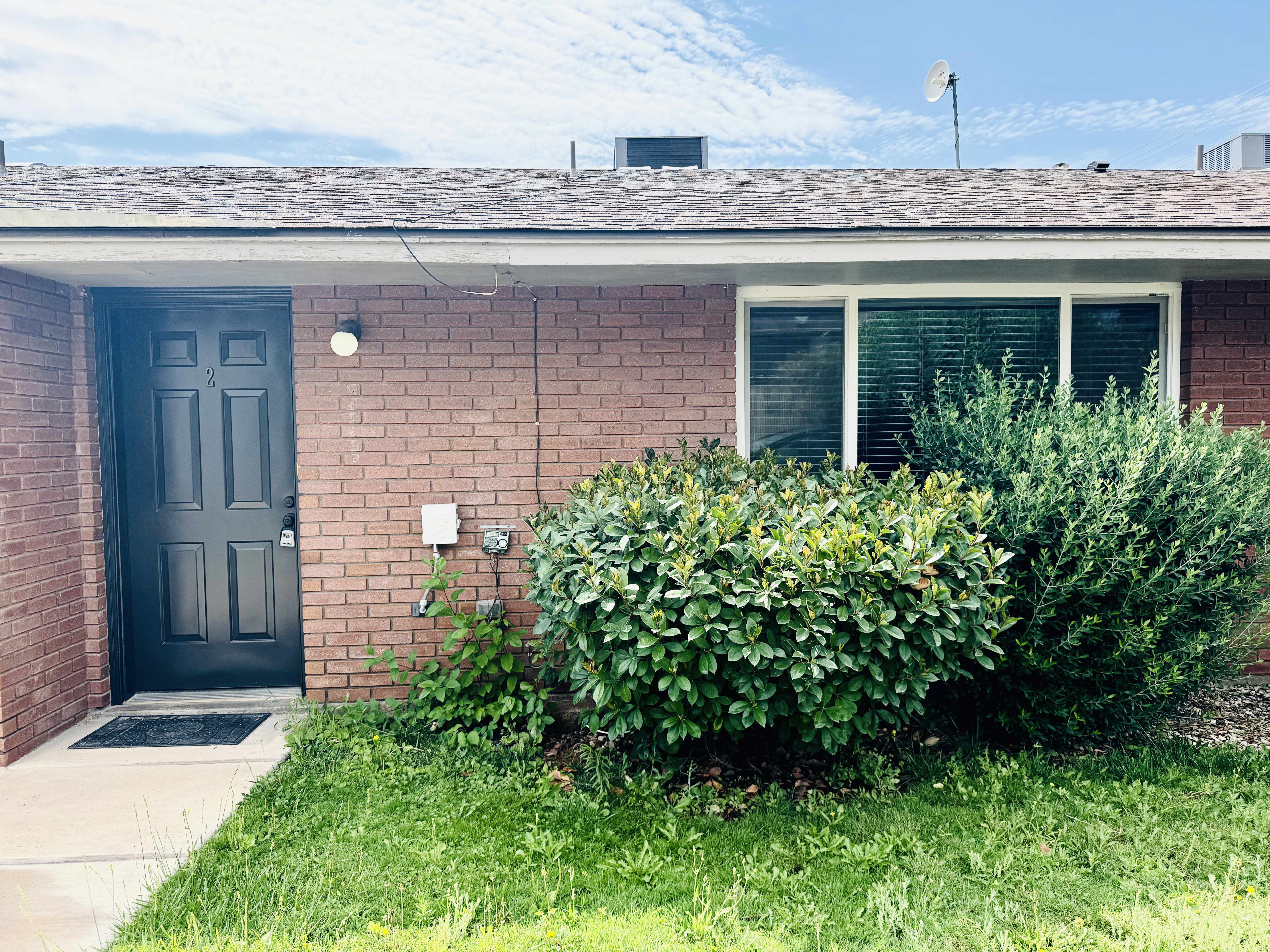 Brick exterior with a dark panel door, a single light fixture, and an adjacent window featuring horizontal blinds