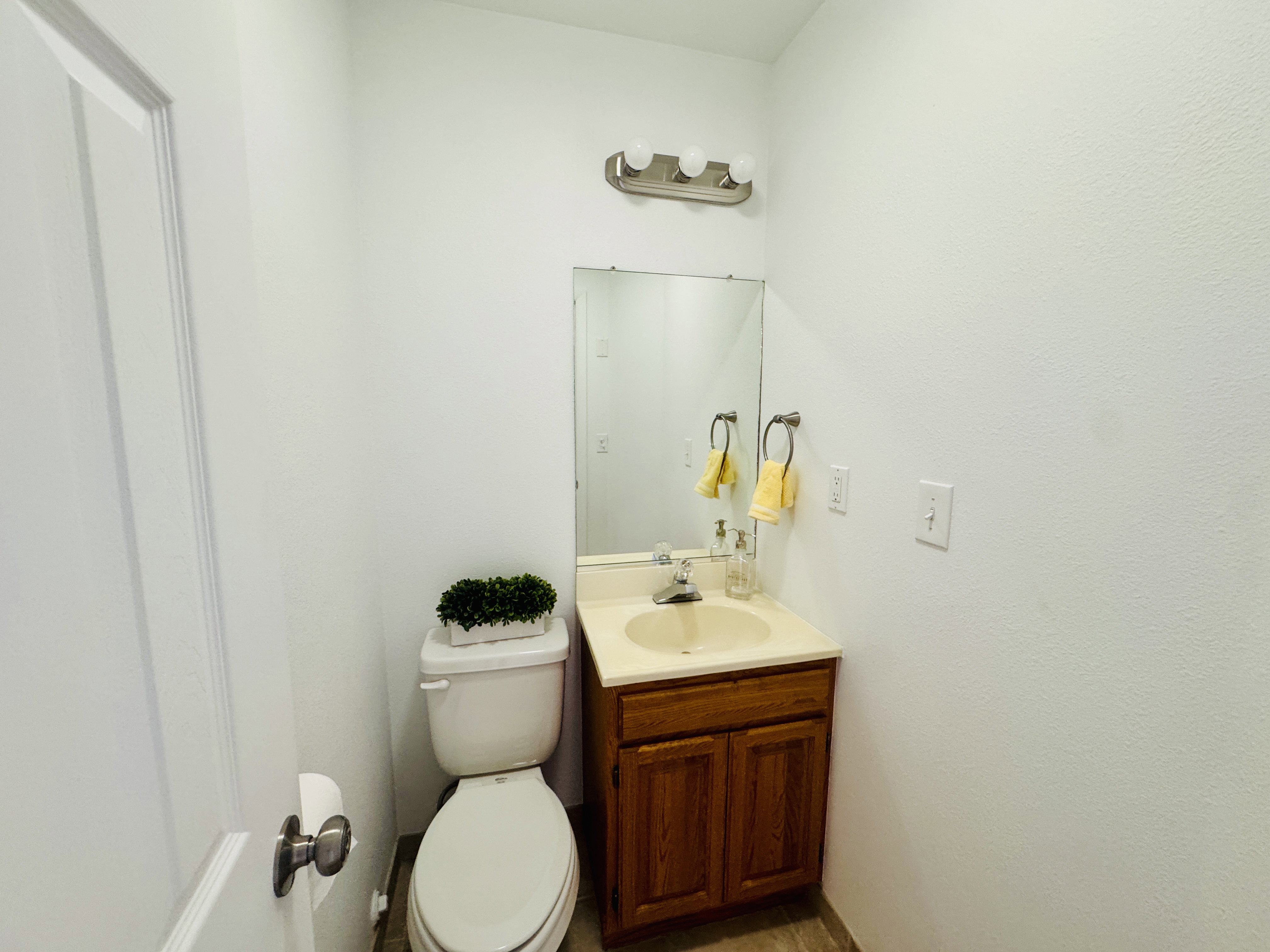 Compact bathroom featuring a white toilet, wood-finish vanity with an integrated sink, and a wall-mounted mirror