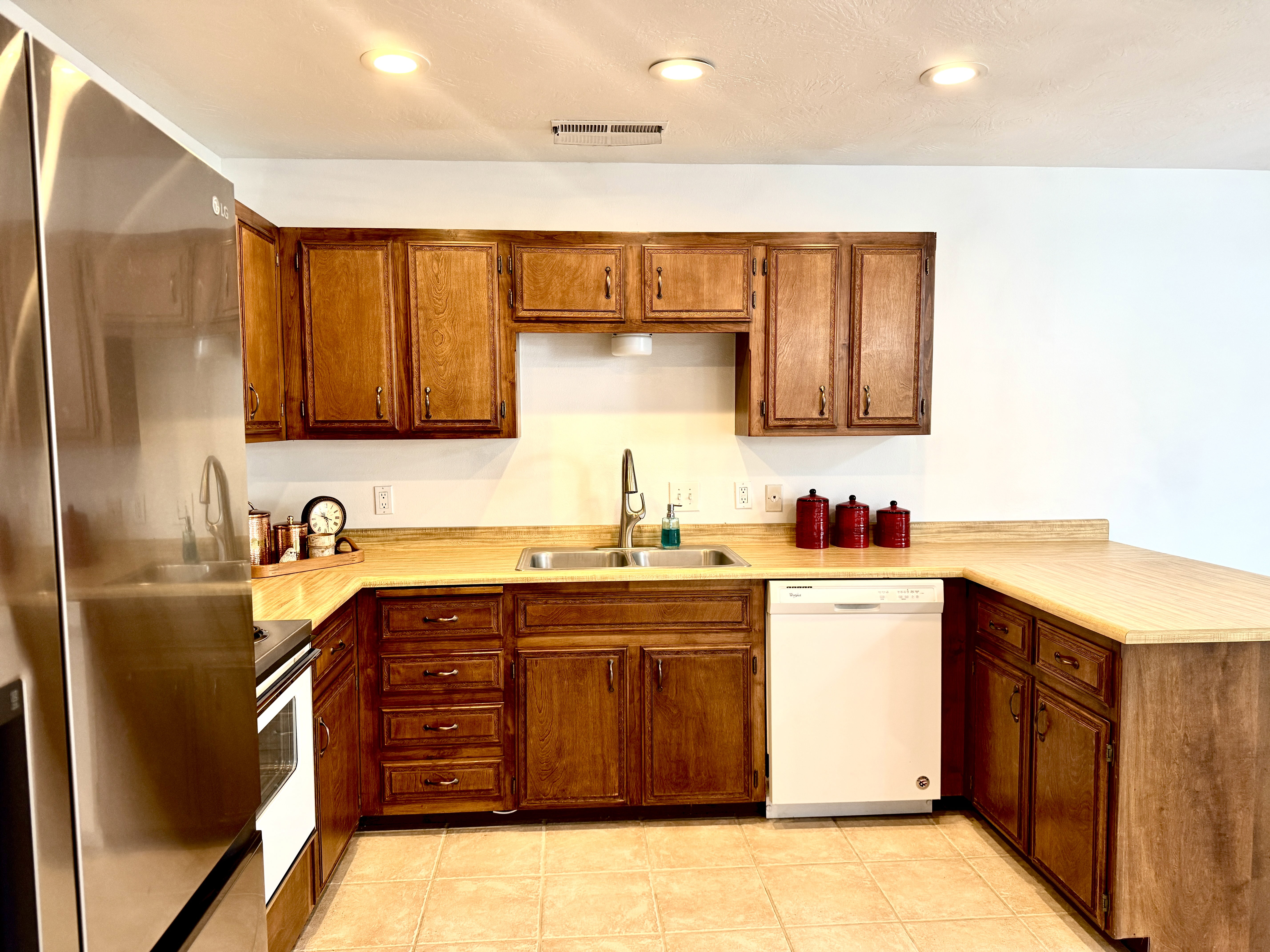 Kitchen featuring wood cabinetry, tan countertops, a double basin sink with a high-arc faucet, integrated dishwasher, and tile flooring