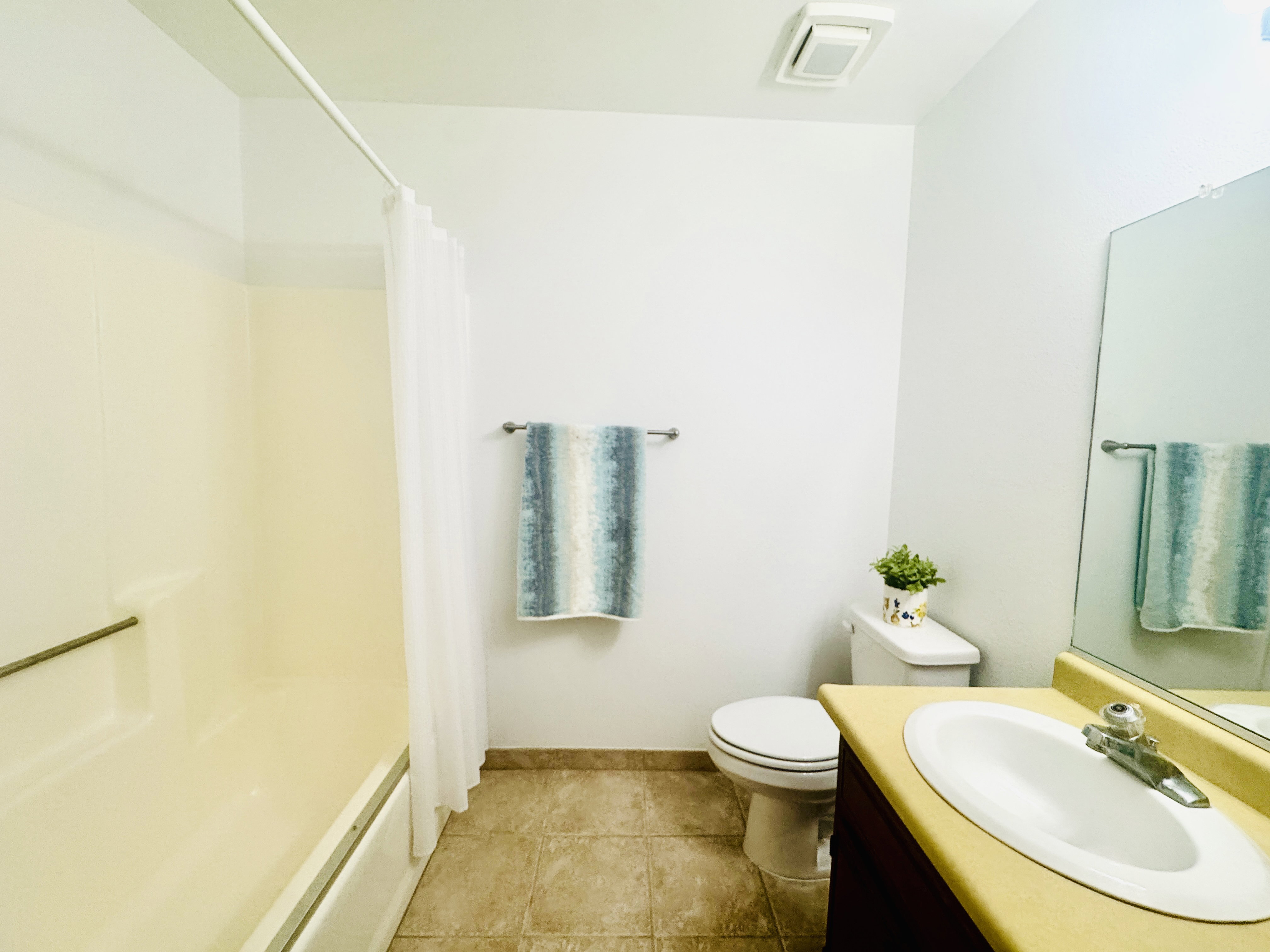 Bathroom featuring a combination bathtub and shower with a grab bar, a single vanity with an integrated sink, a wall-mounted mirror, ceramic tile flooring, and a ceiling-mounted exhaust fan