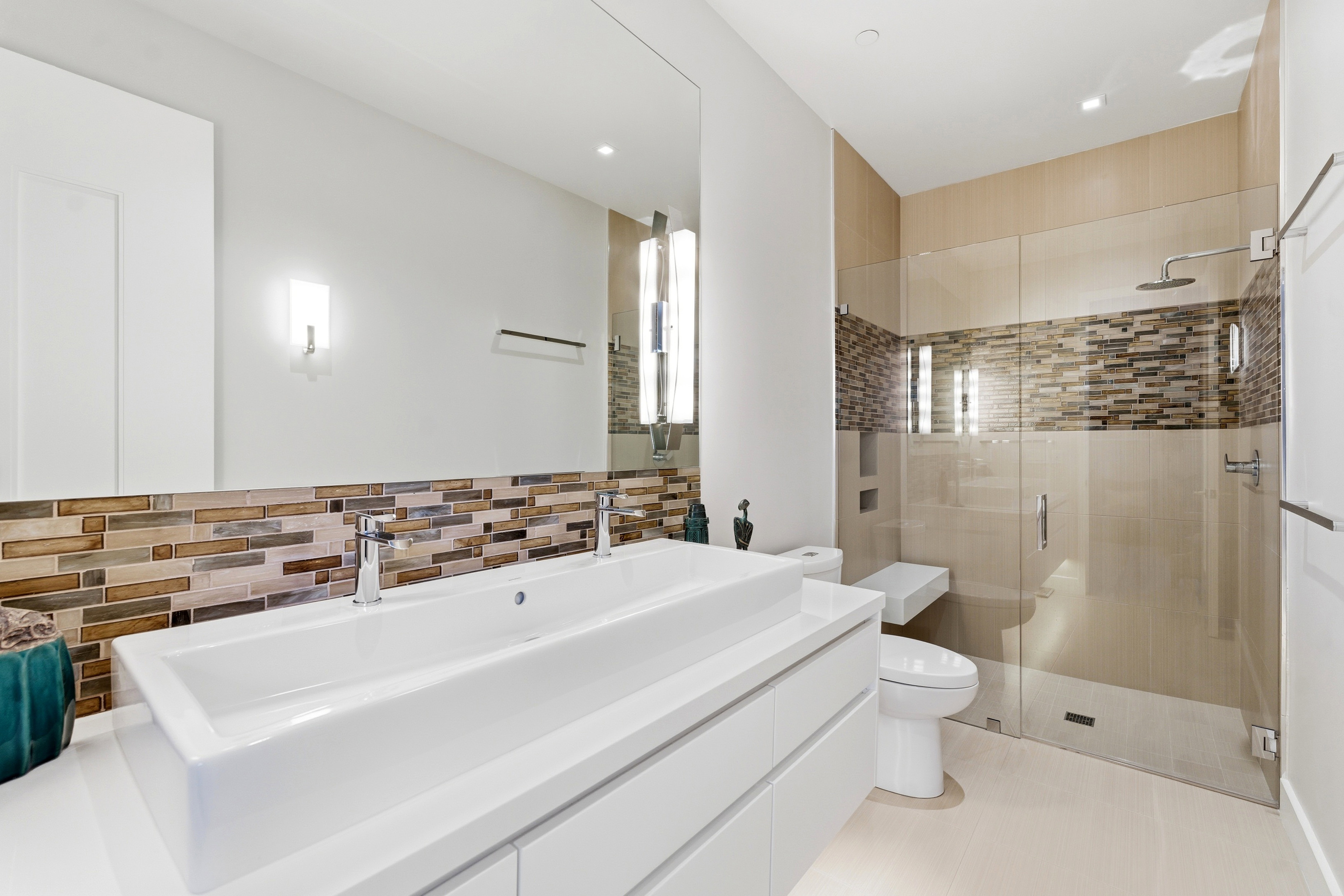 Contemporary bathroom featuring a dual vanity with rectangular vessel sinks, extensive mirrored wall, glass-enclosed shower with a built-in bench, and a mosaic tile accent band