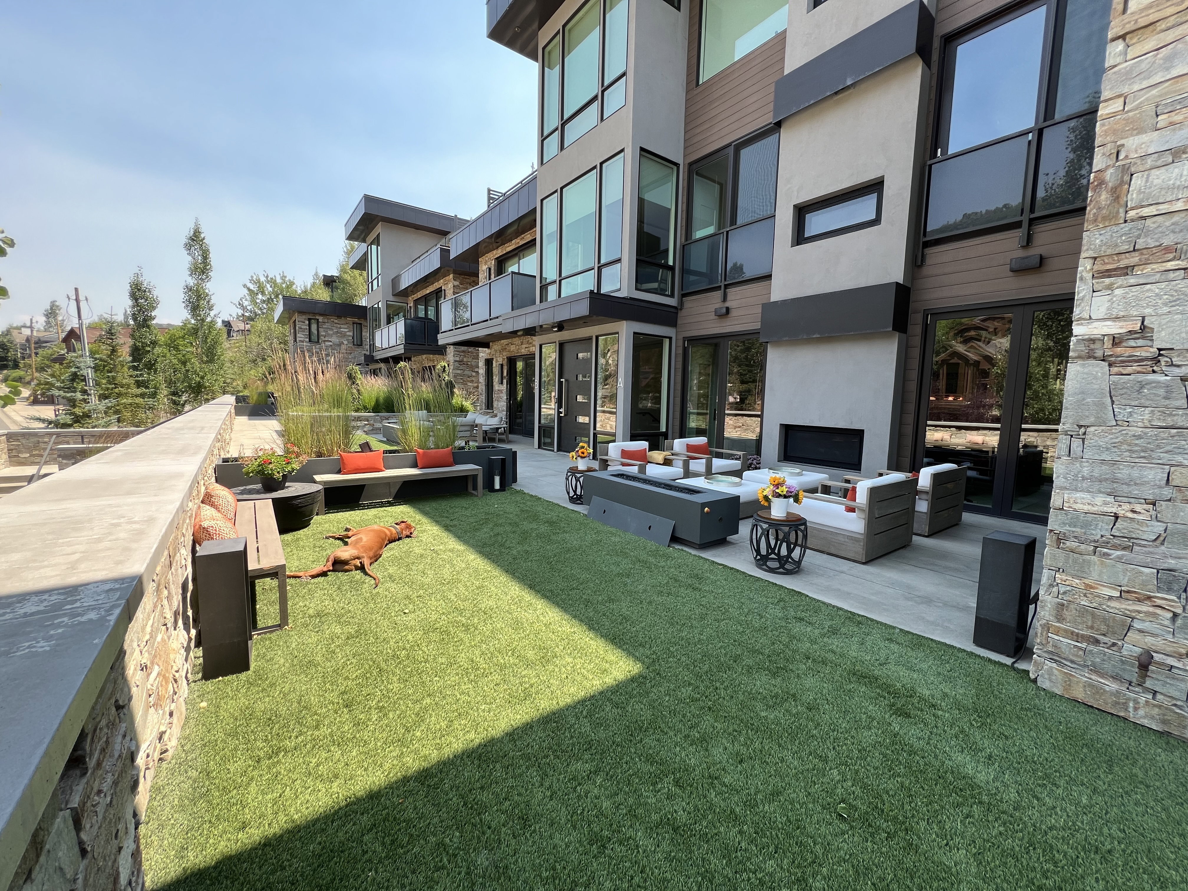 Outdoor living area featuring a stone accent wall, artificial turf lawn, and a paved patio