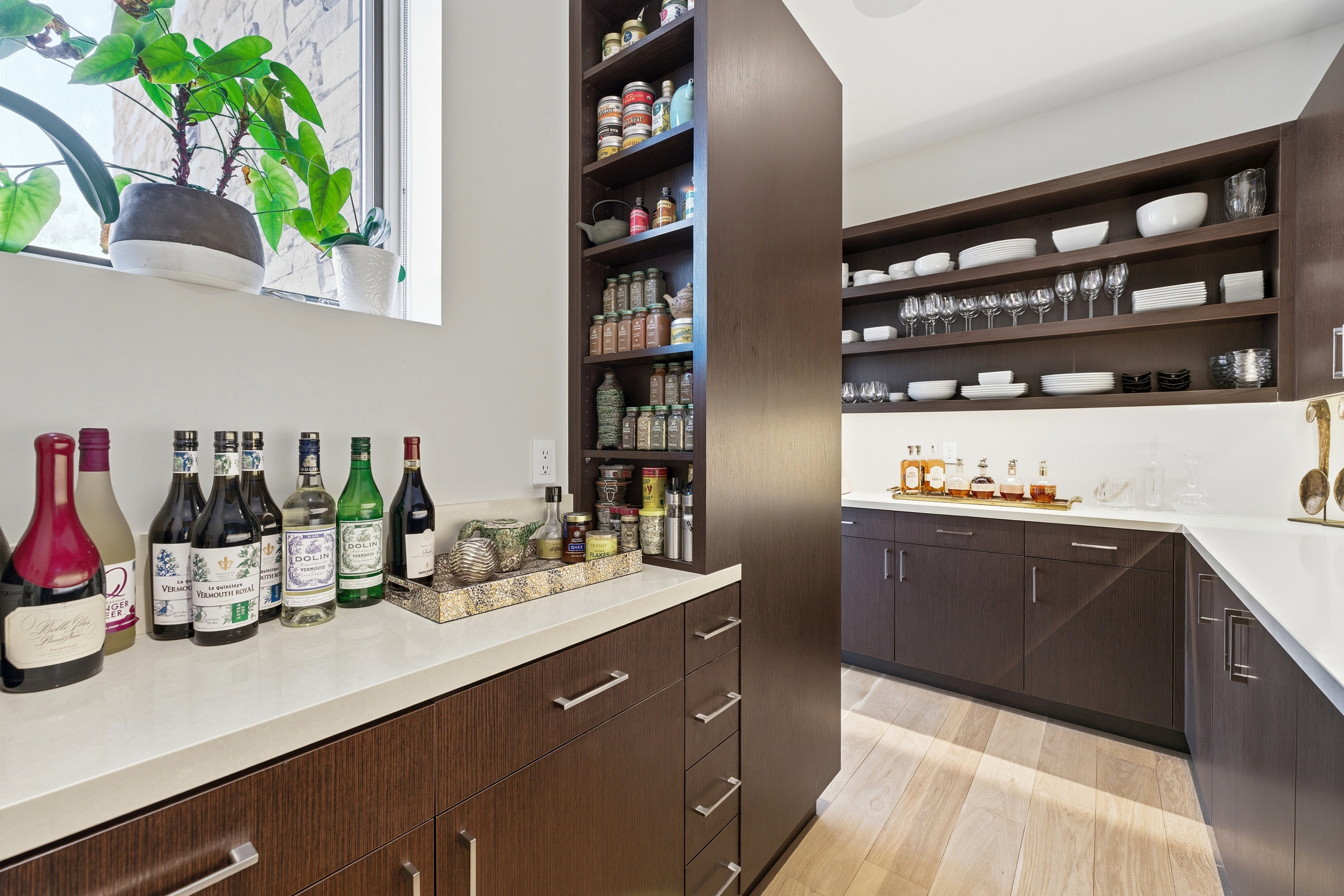 Custom pantry featuring extensive dark wood-finish cabinetry, light-toned countertops, open shelving, integrated shelving units, and a window with natural light