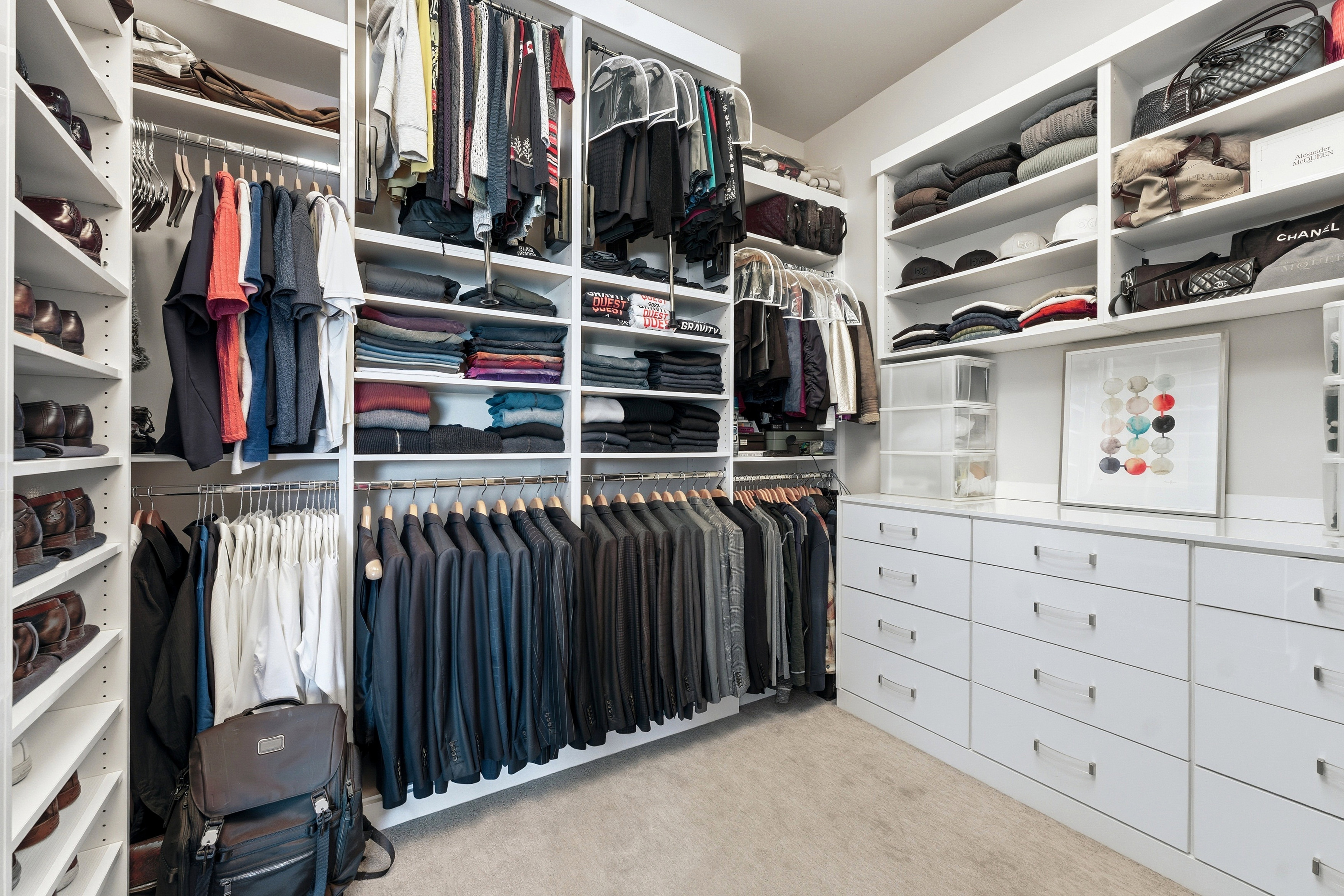 Custom closet system featuring extensive built-in shelving, multiple hanging rods, integrated drawer storage, and a light-colored carpeted floor
