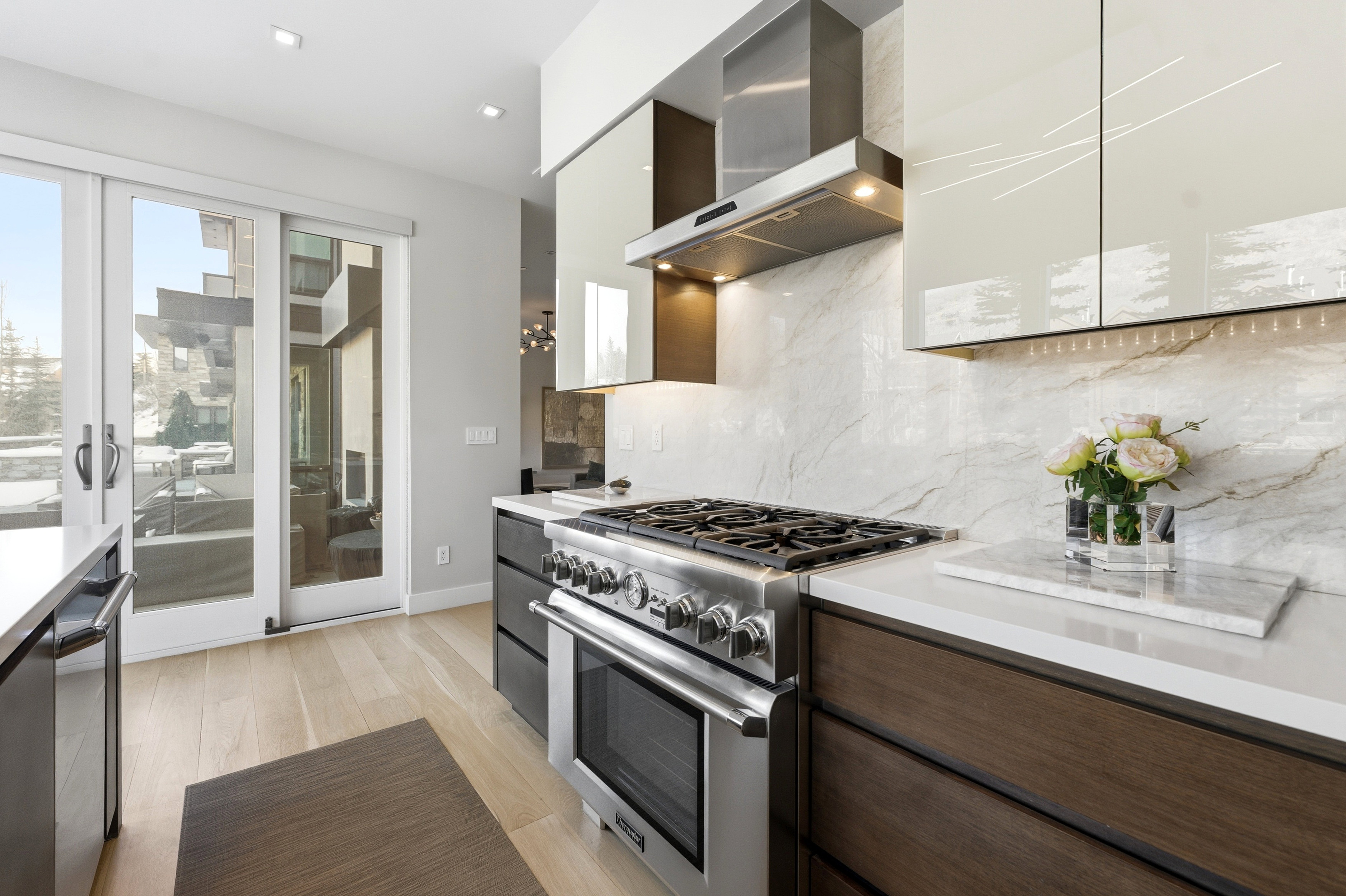Gourmet kitchen featuring a stainless steel range with a ventilation hood, light-toned wood-finish flooring, white countertops, a stone-finish backsplash, and modern cabinetry