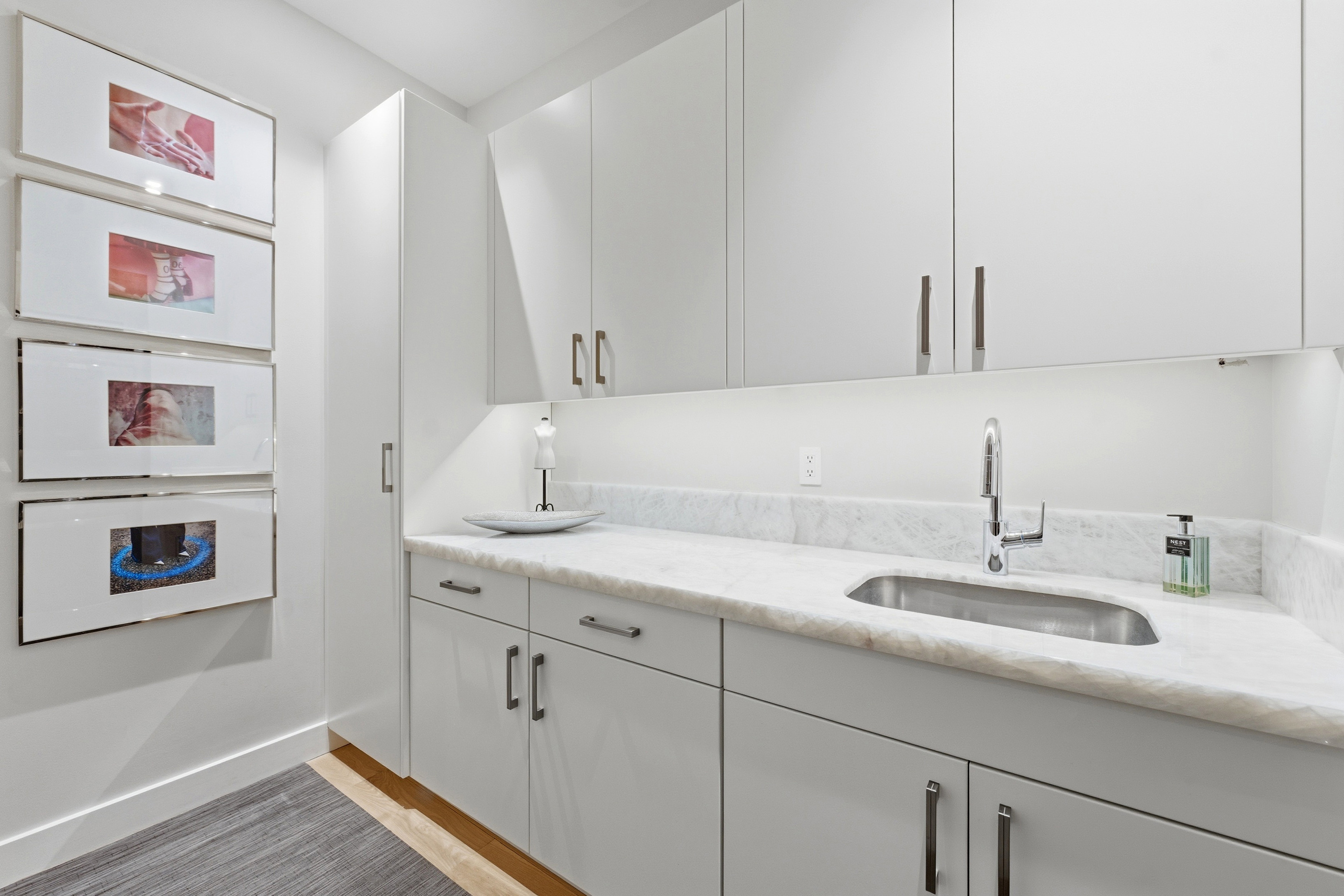 Contemporary white cabinetry with brushed nickel hardware, undermount stainless steel sink, natural stone countertop, and under-cabinet lighting
