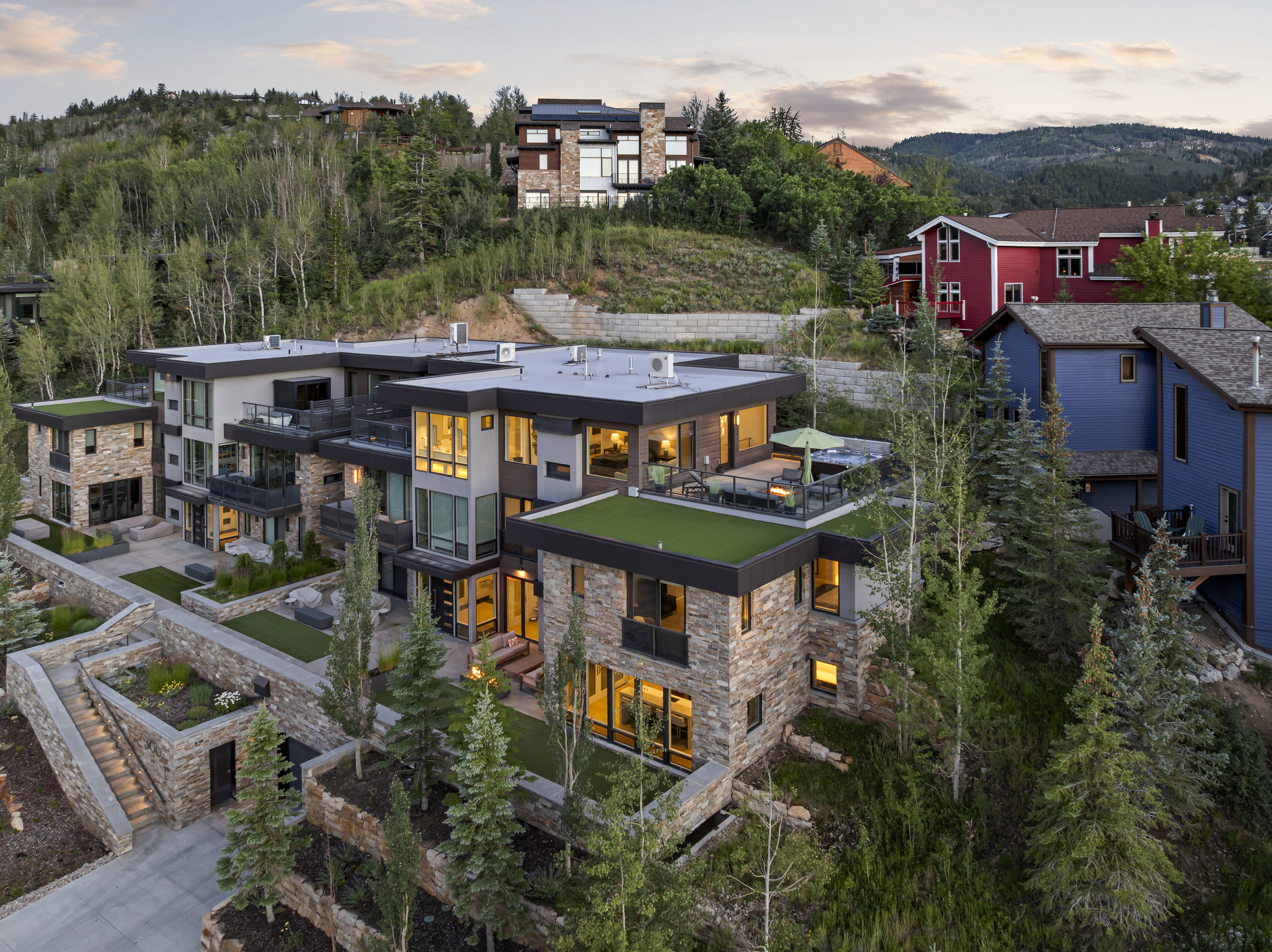 Contemporary multi-level residence featuring stone and stucco facade, multiple exterior terraces, green roof accents, and landscaped grounds with mature trees