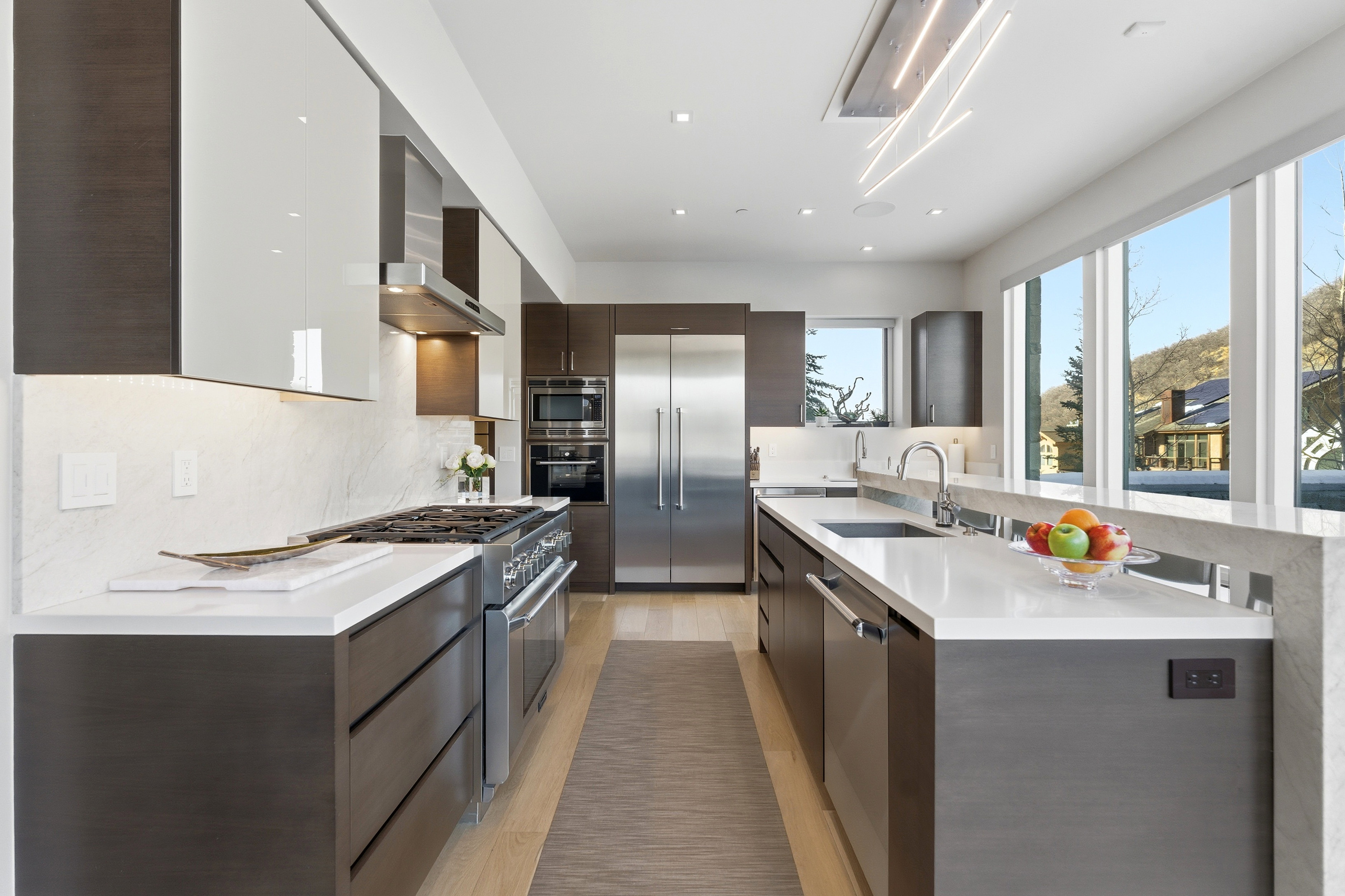 Modern kitchen featuring wood-finish lower cabinetry, white upper cabinetry, and a full suite of stainless steel appliances