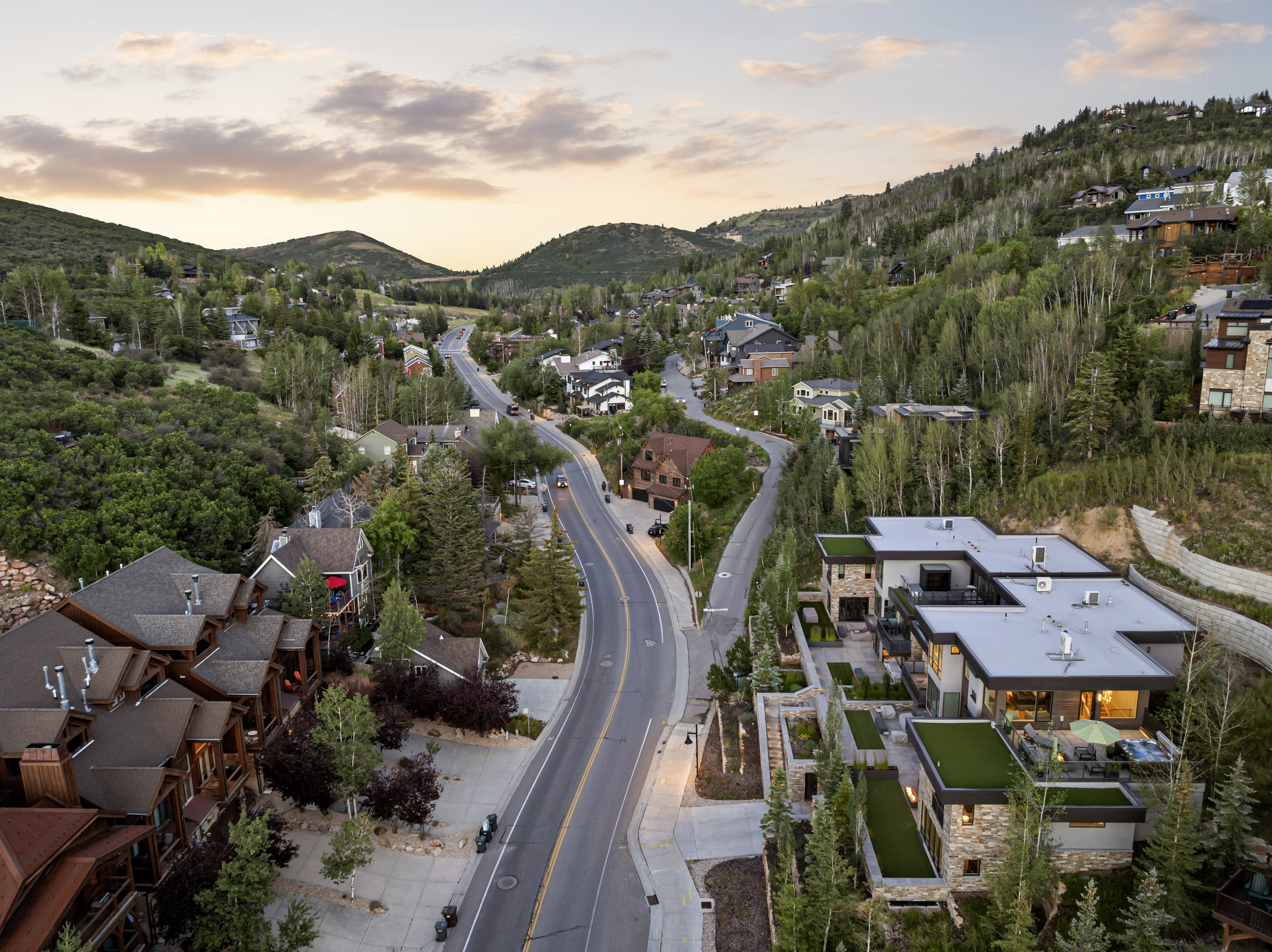 Modern mountain residence featuring a stone and stucco facade, multiple levels of outdoor living space, integrated artificial turf terraces, and a flat roof design