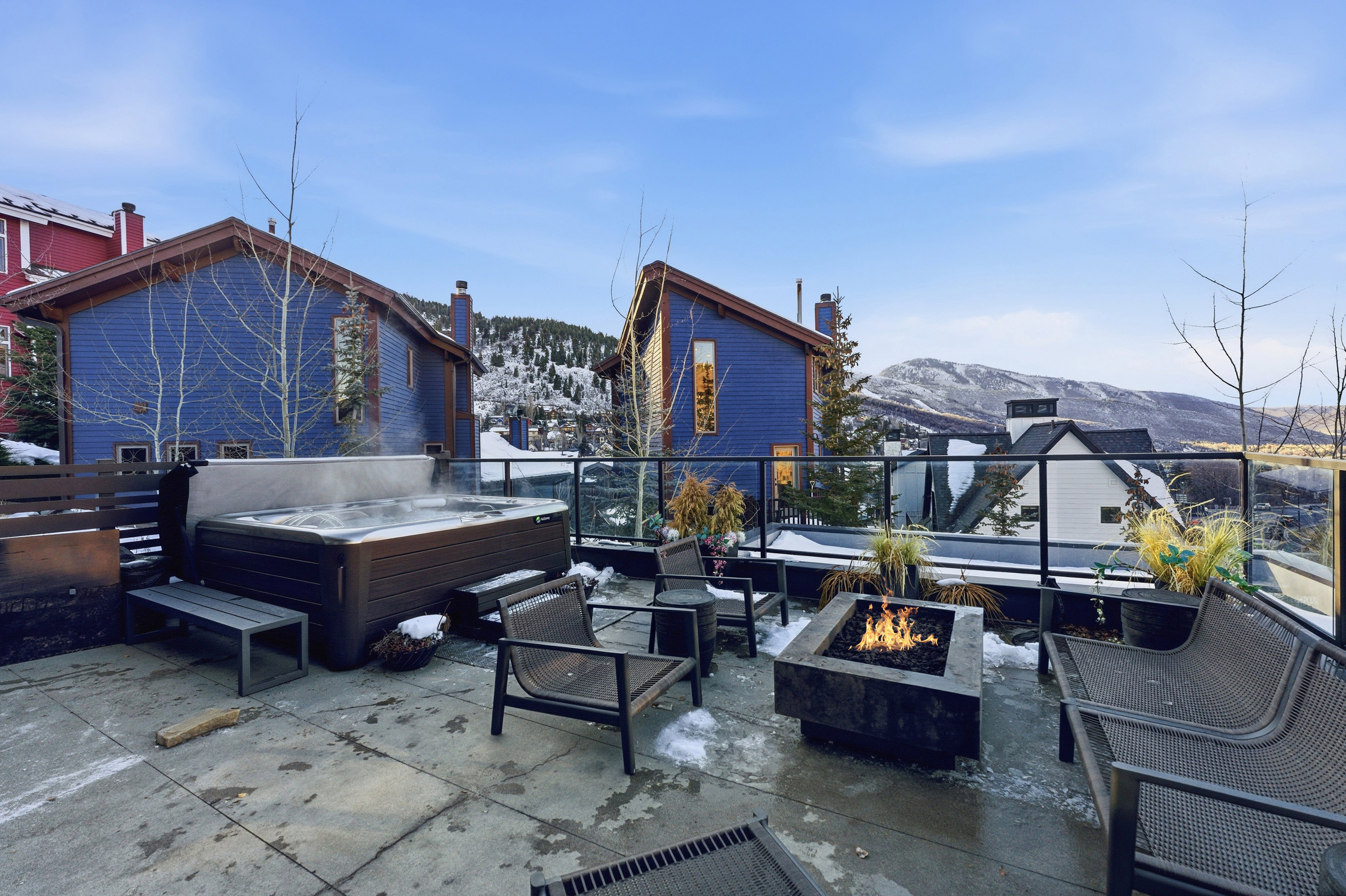 Spacious outdoor patio featuring a hot tub, a built-in fire pit, and a glass-paneled railing