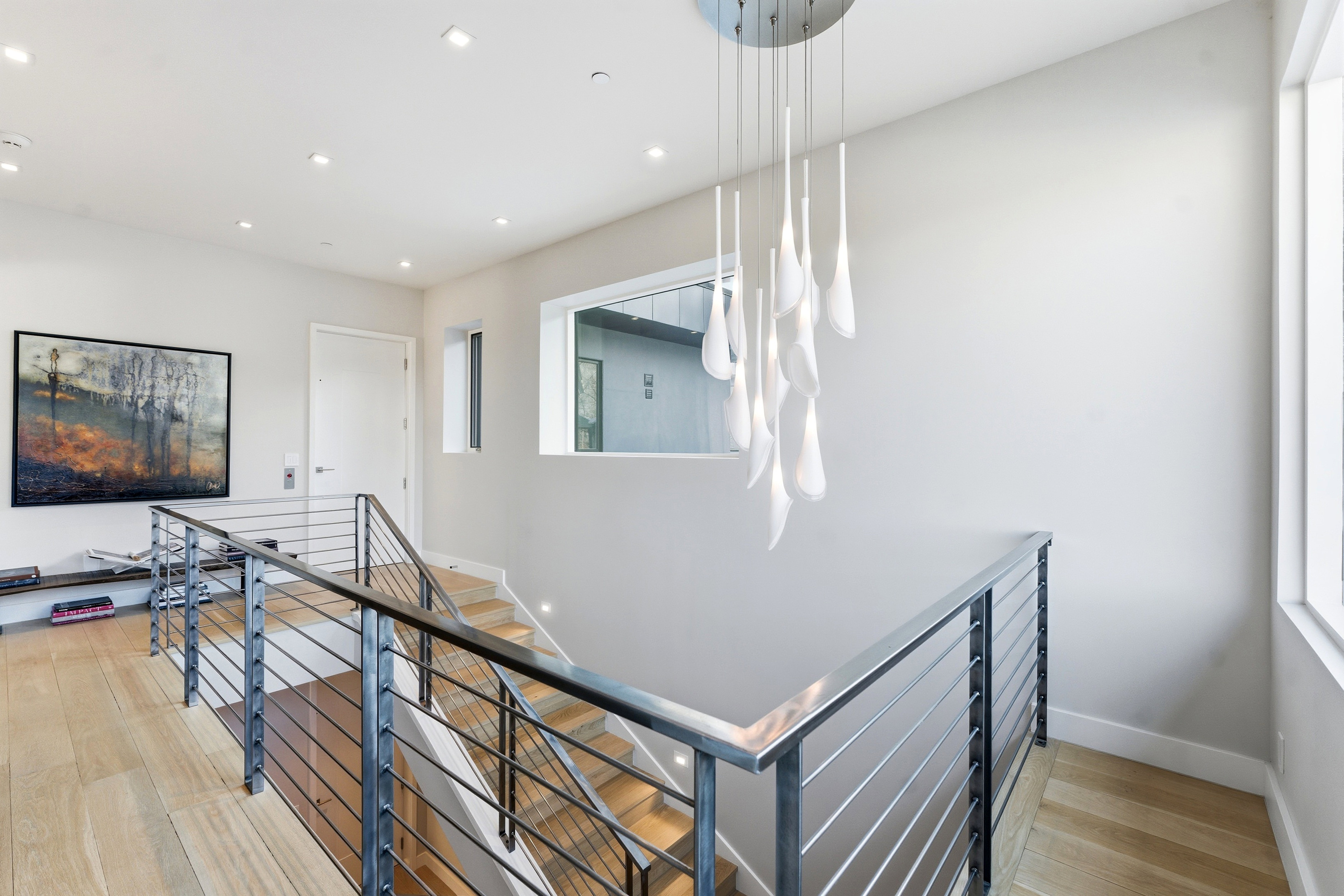 Modern staircase featuring a sleek metal railing with horizontal balusters, wood-finish flooring, and recessed ceiling lighting