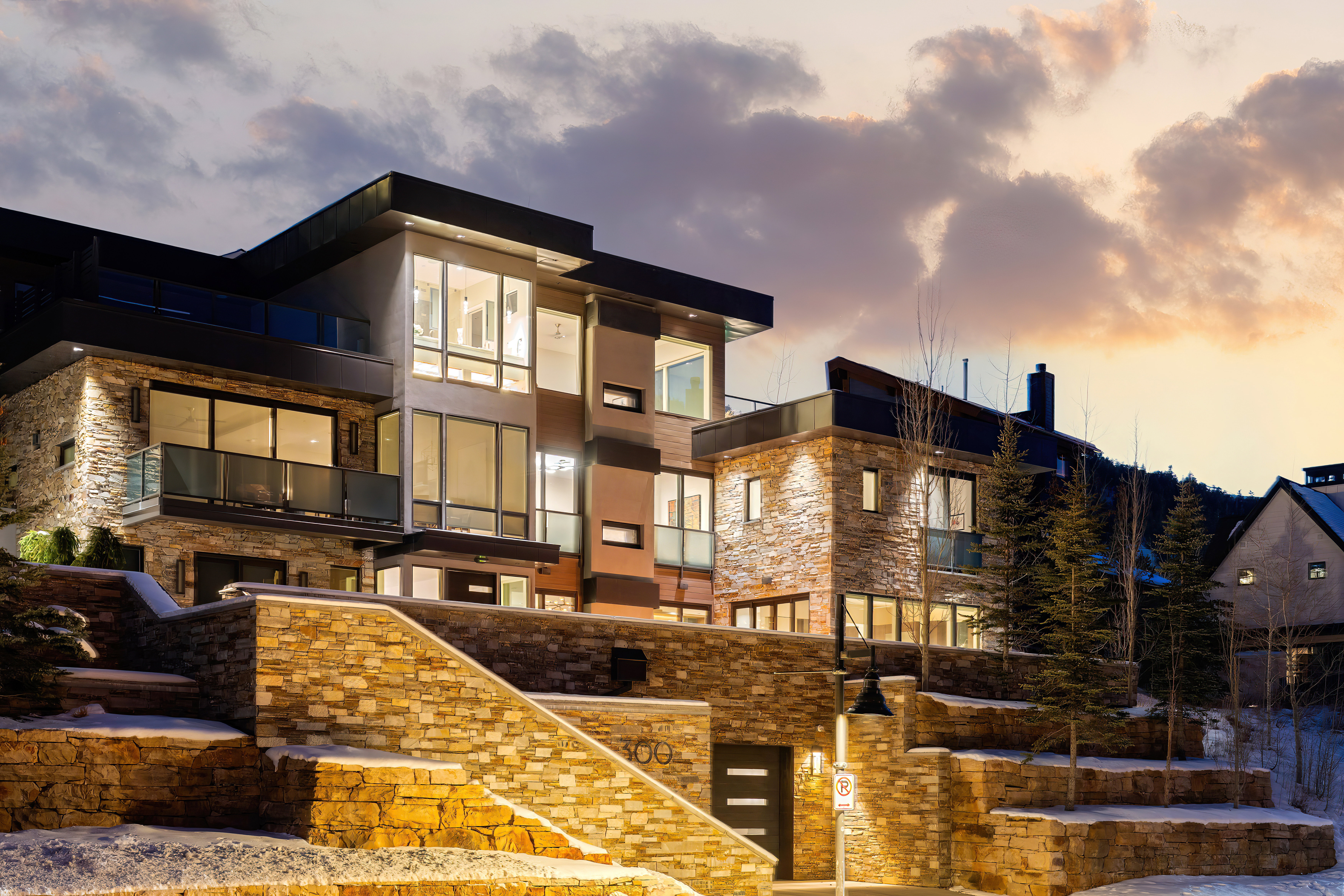 Multi-level modern residence featuring extensive stone veneer siding, large pane windows, and multiple private balconies with glass railings