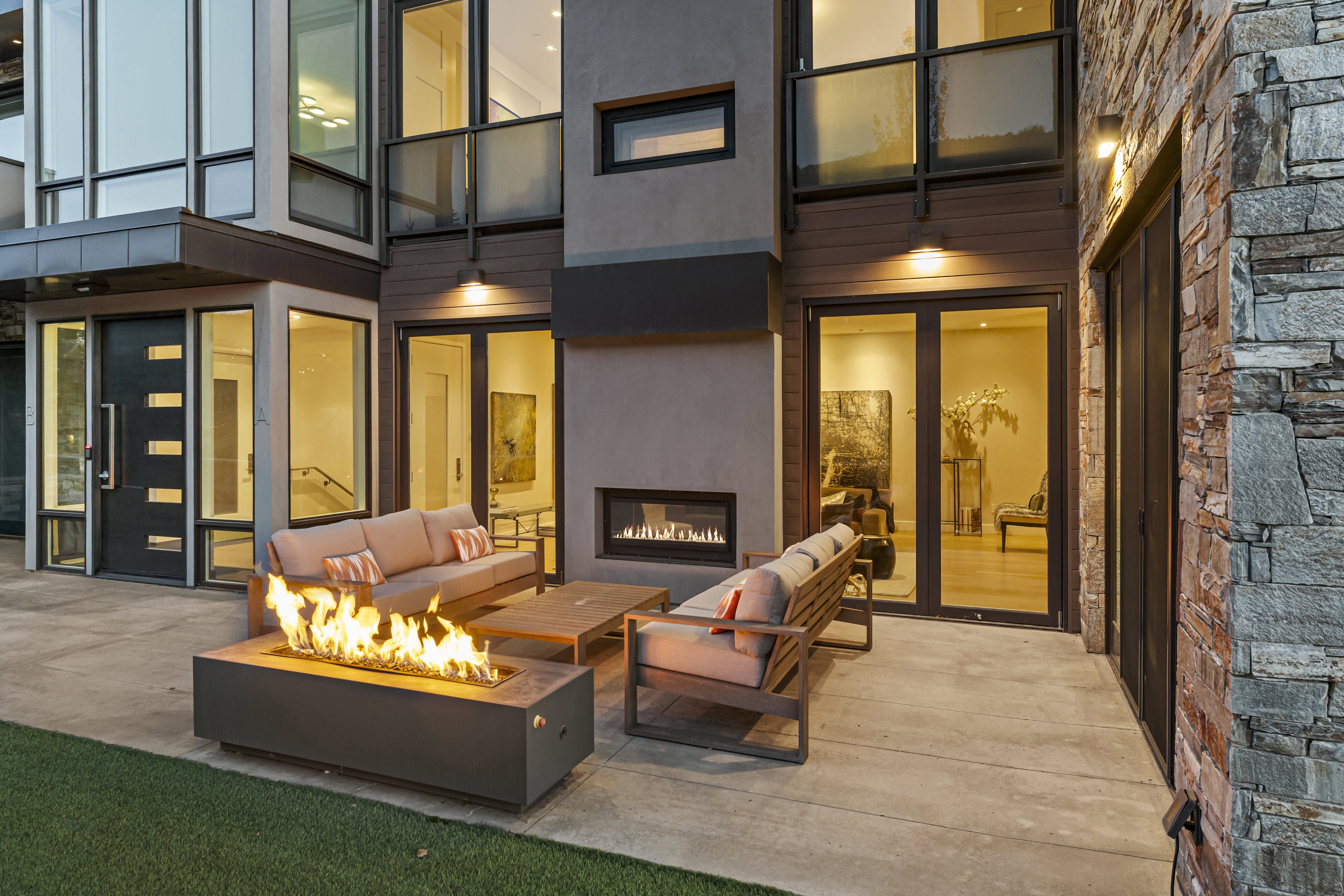 Spacious concrete patio featuring a modern fire pit, an outdoor fireplace, and multiple floor-to-ceiling windows