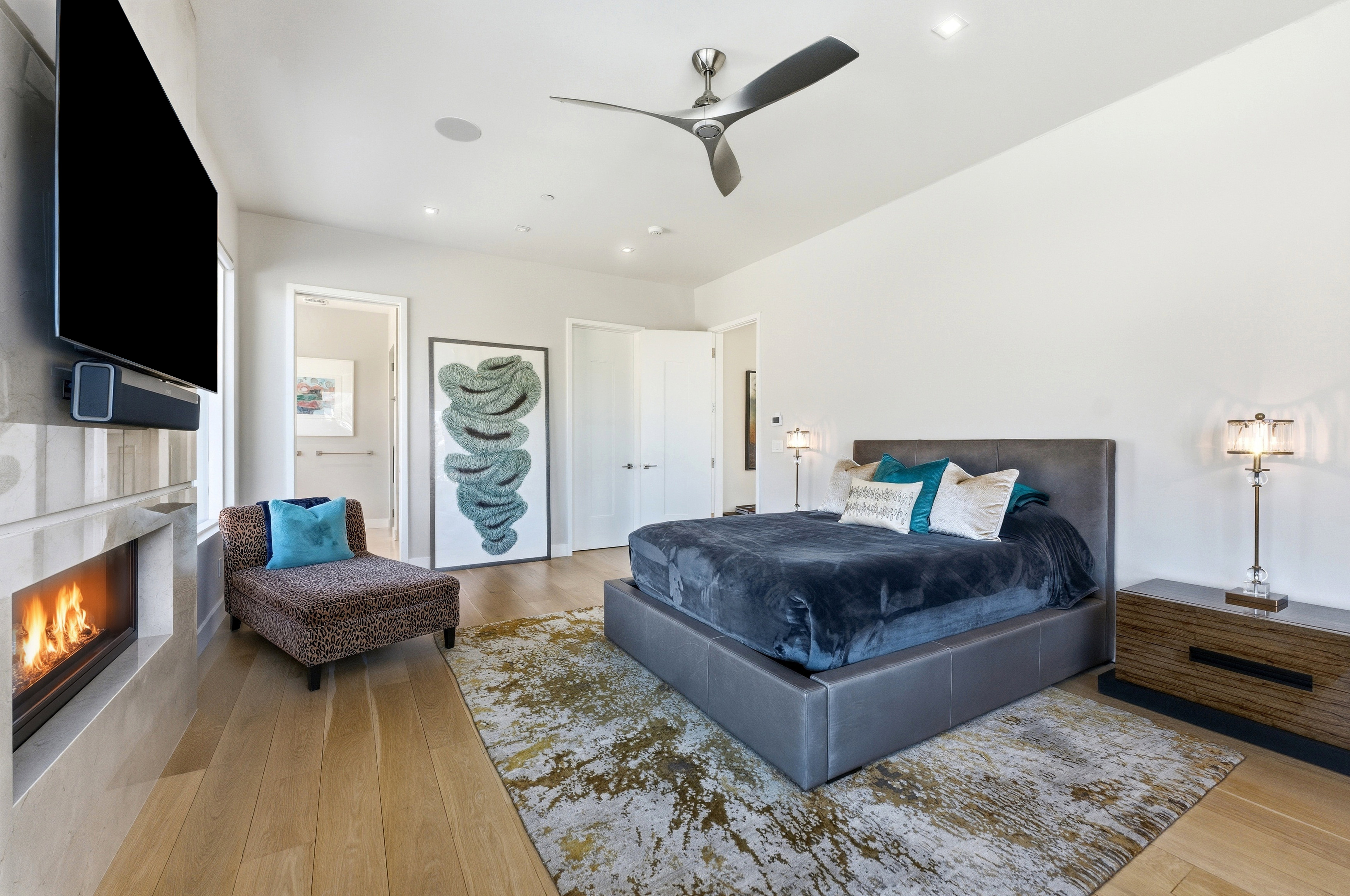 Spacious room featuring wood-finish flooring, a wall-mounted fireplace with an integrated television, and a contemporary ceiling fan