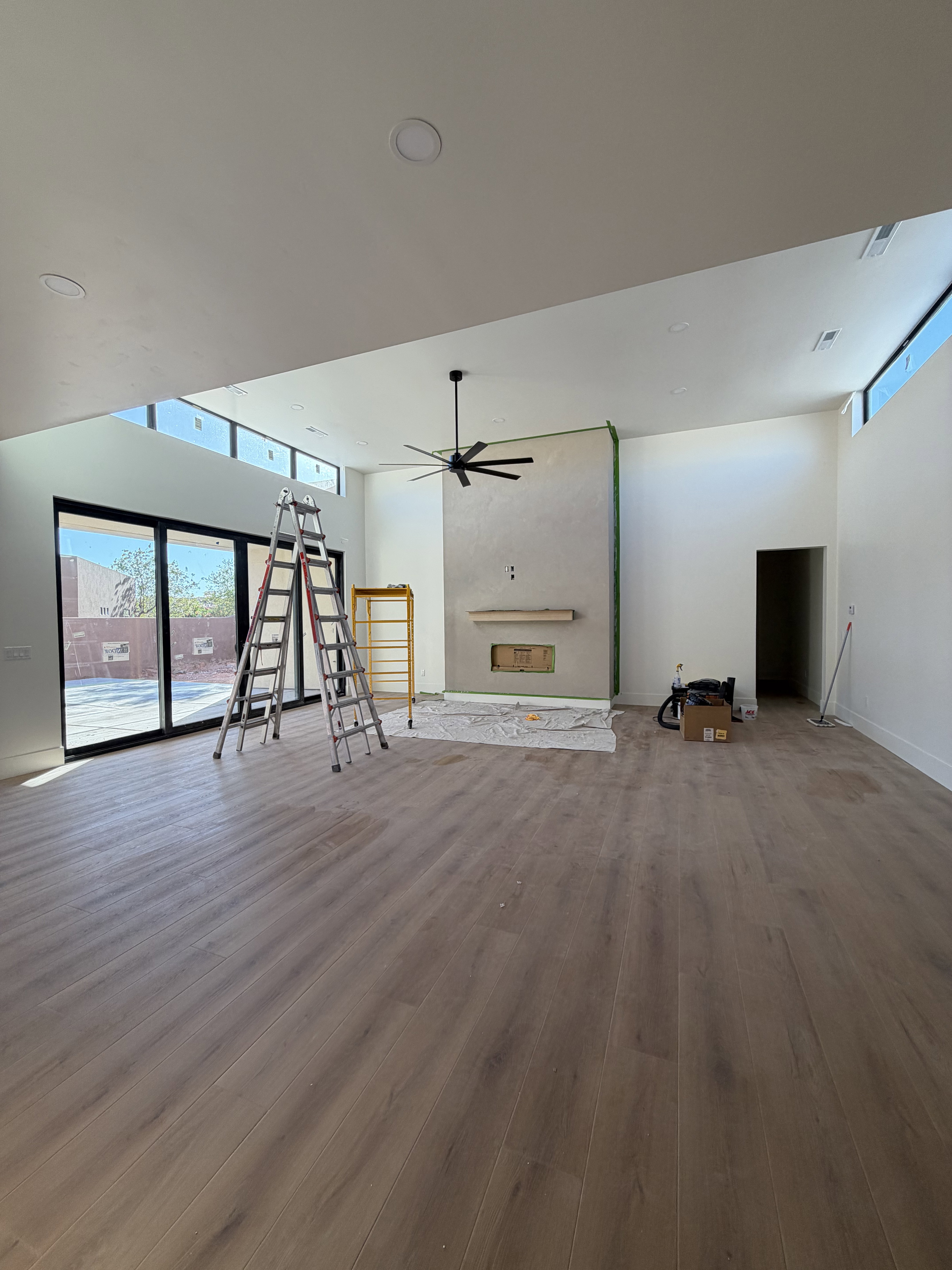 Expansive living area featuring wood-finish flooring, a contemporary fireplace with a wood mantle, and a modern ceiling fan