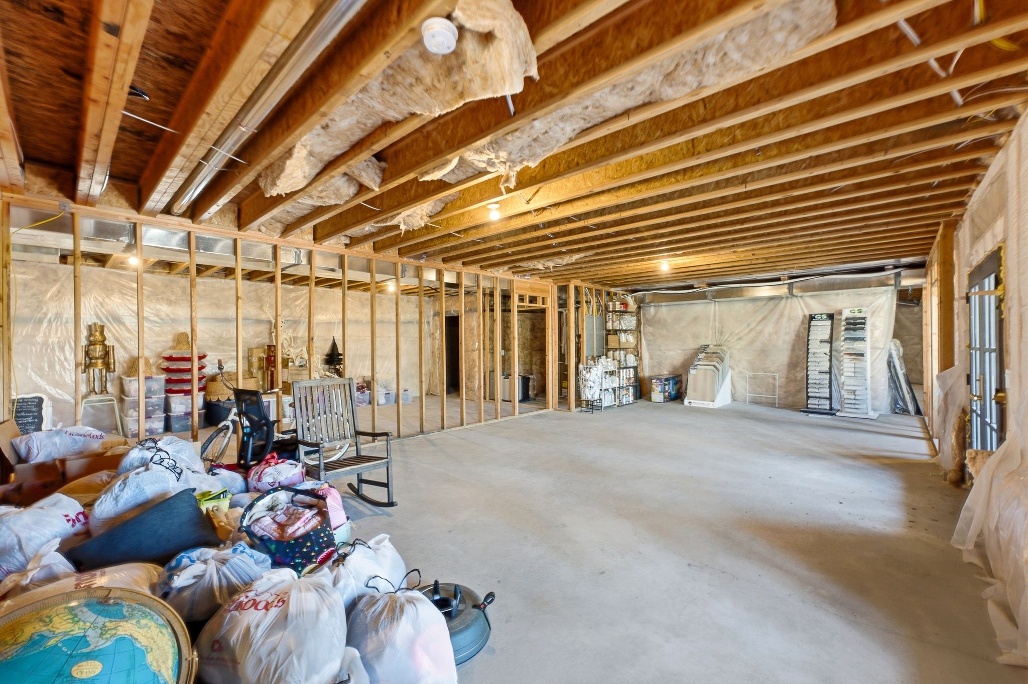 Unfinished basement featuring exposed wood framing, concrete flooring, and an open ceiling with visible insulation