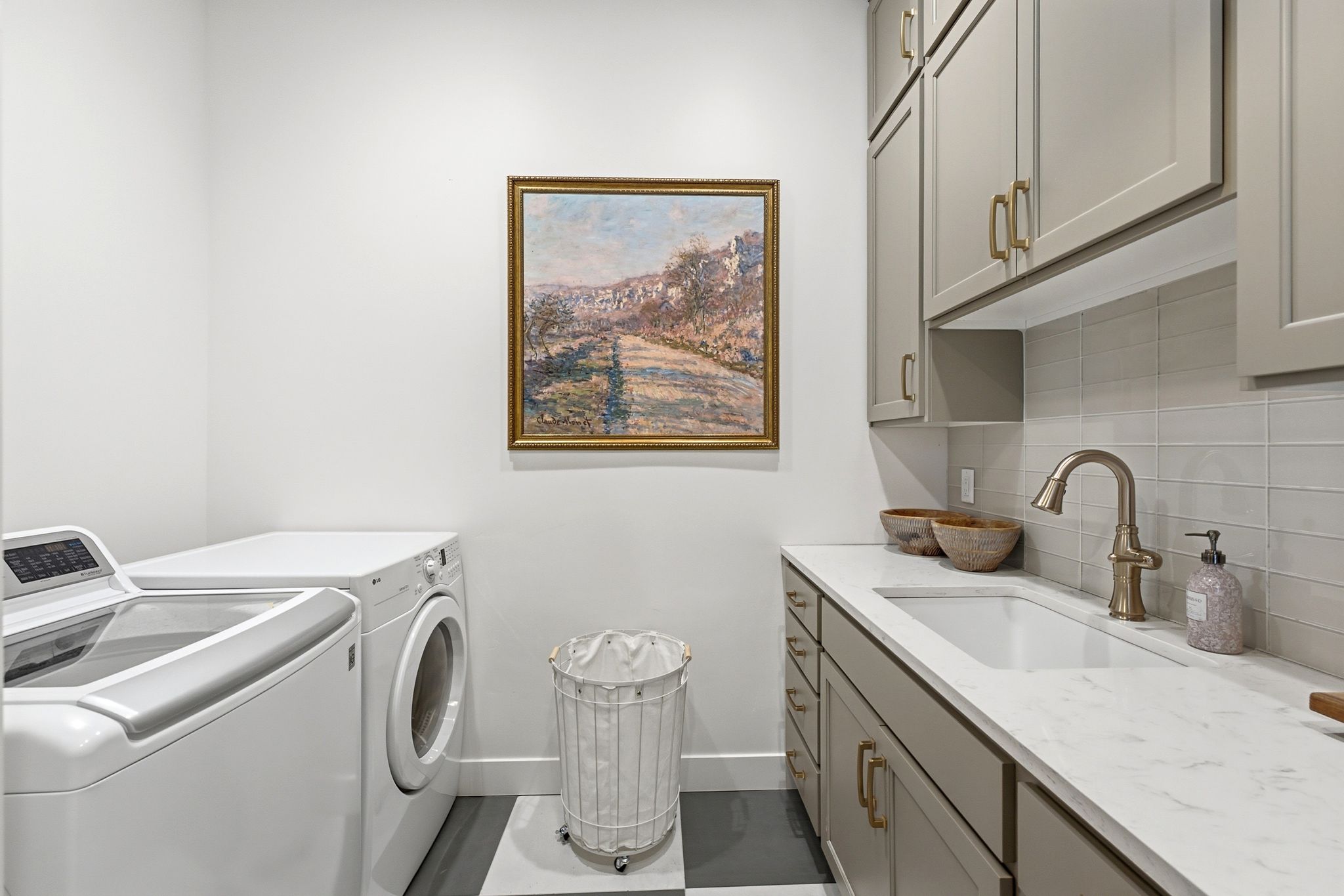 Laundry area featuring extensive upper and lower cabinetry, a white countertop, an undermount sink with a gooseneck faucet, and a light-toned tile backsplash