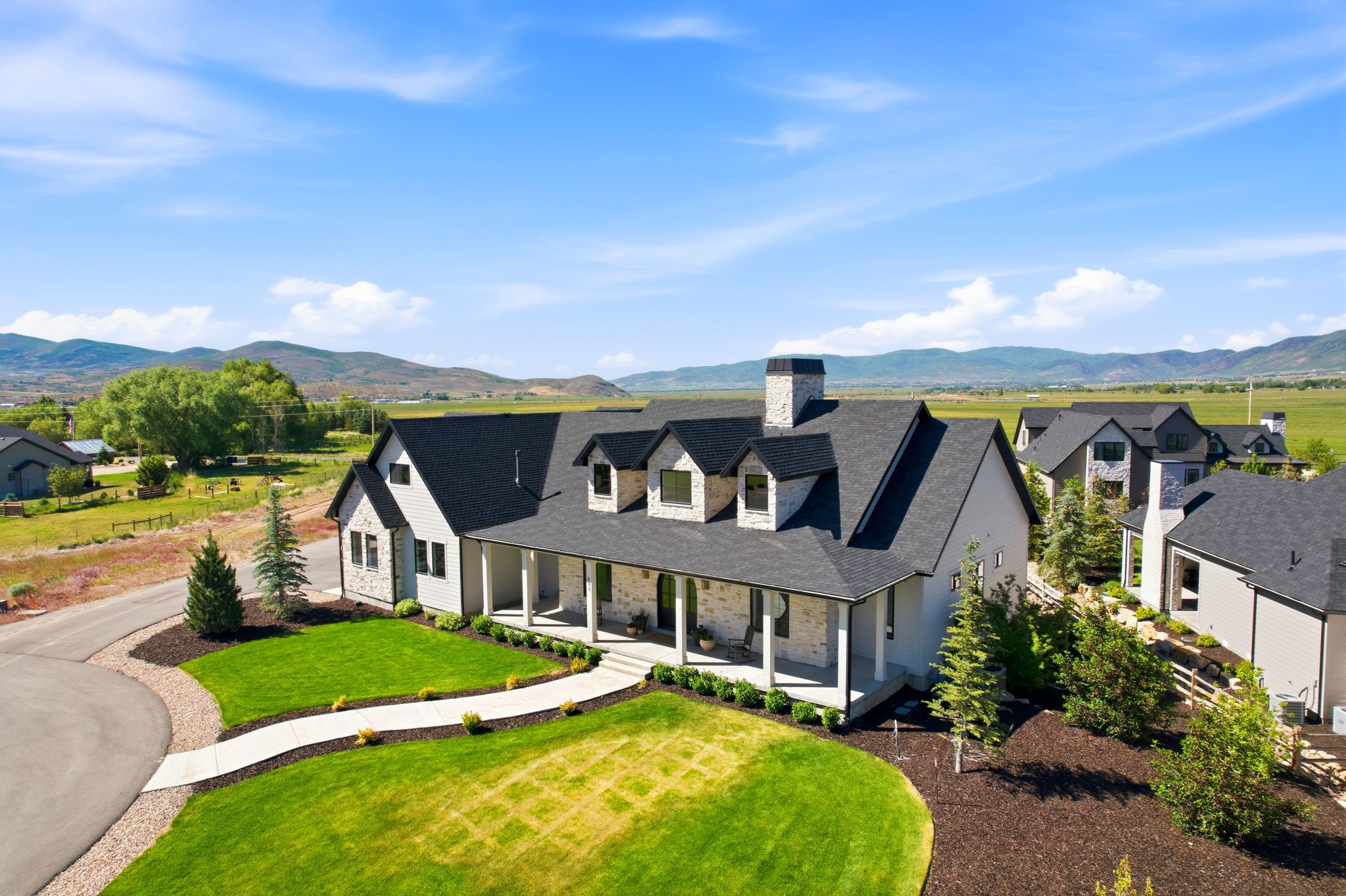 Contemporary farmhouse style residence featuring a stone and stucco exterior, prominent gables, and dormer windows