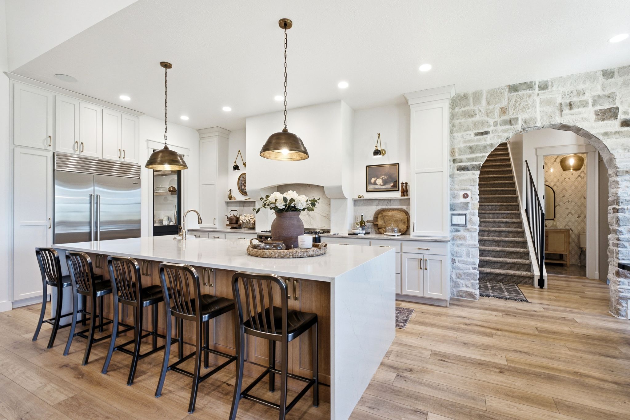 Gourmet kitchen featuring a large central island with seating, stainless steel built-in appliances, custom cabinetry, a stone accent wall, and wood-finish flooring