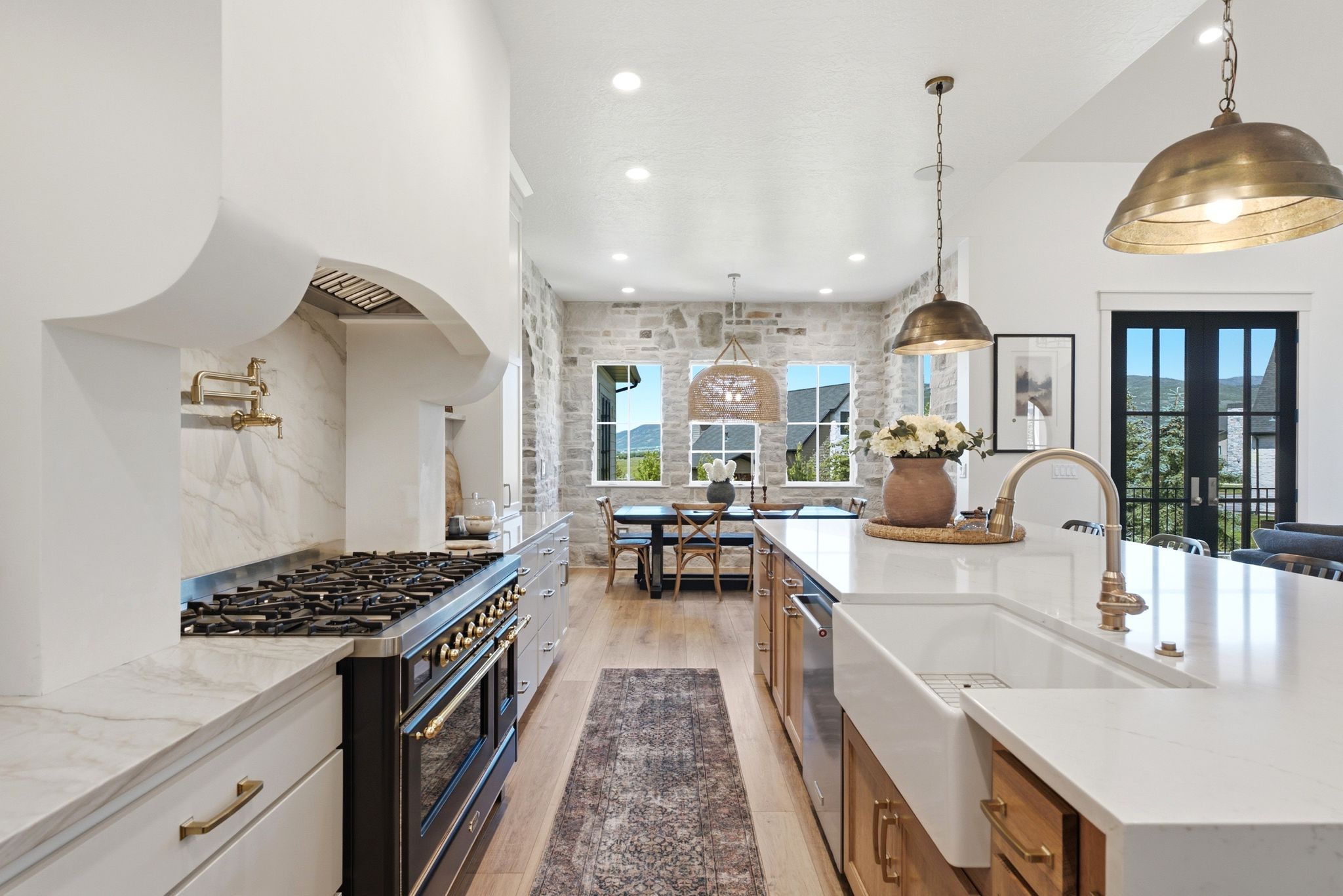Expansive kitchen featuring a large island with a farmhouse sink, stone accent wall, wood-finish flooring, a range with a pot filler, and recessed lighting