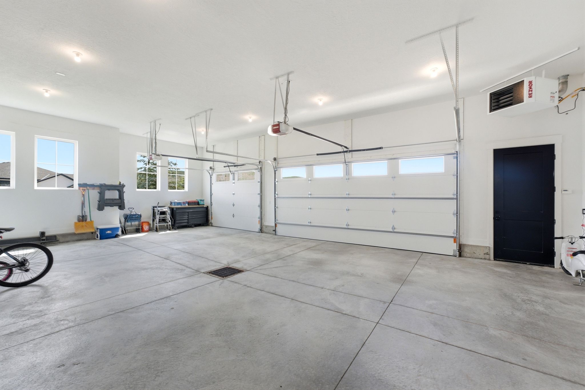 Spacious garage featuring a concrete floor, multiple windows, two overhead garage doors with window panels, recessed lighting, and a dark-paneled side door