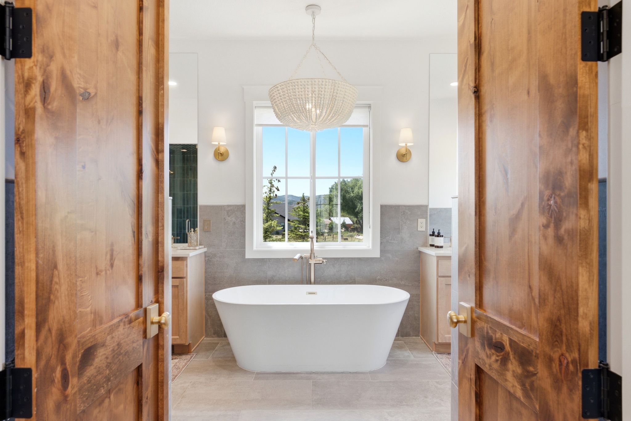 Freestanding soaking tub centered under a window, flanked by two wood-finish vanity cabinets with undermount sinks